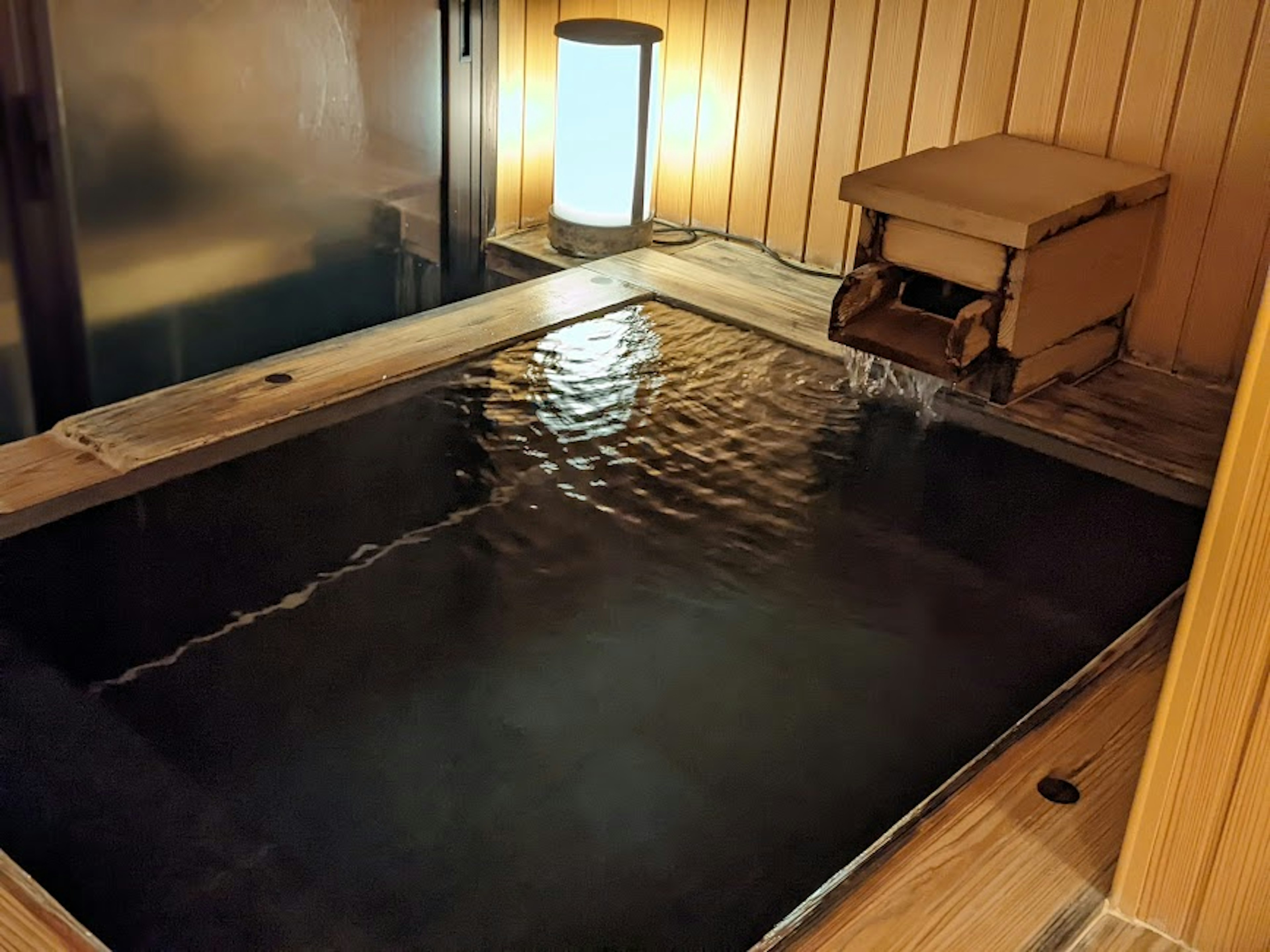 Wooden soaking tub filled with warm water and a softly glowing lamp