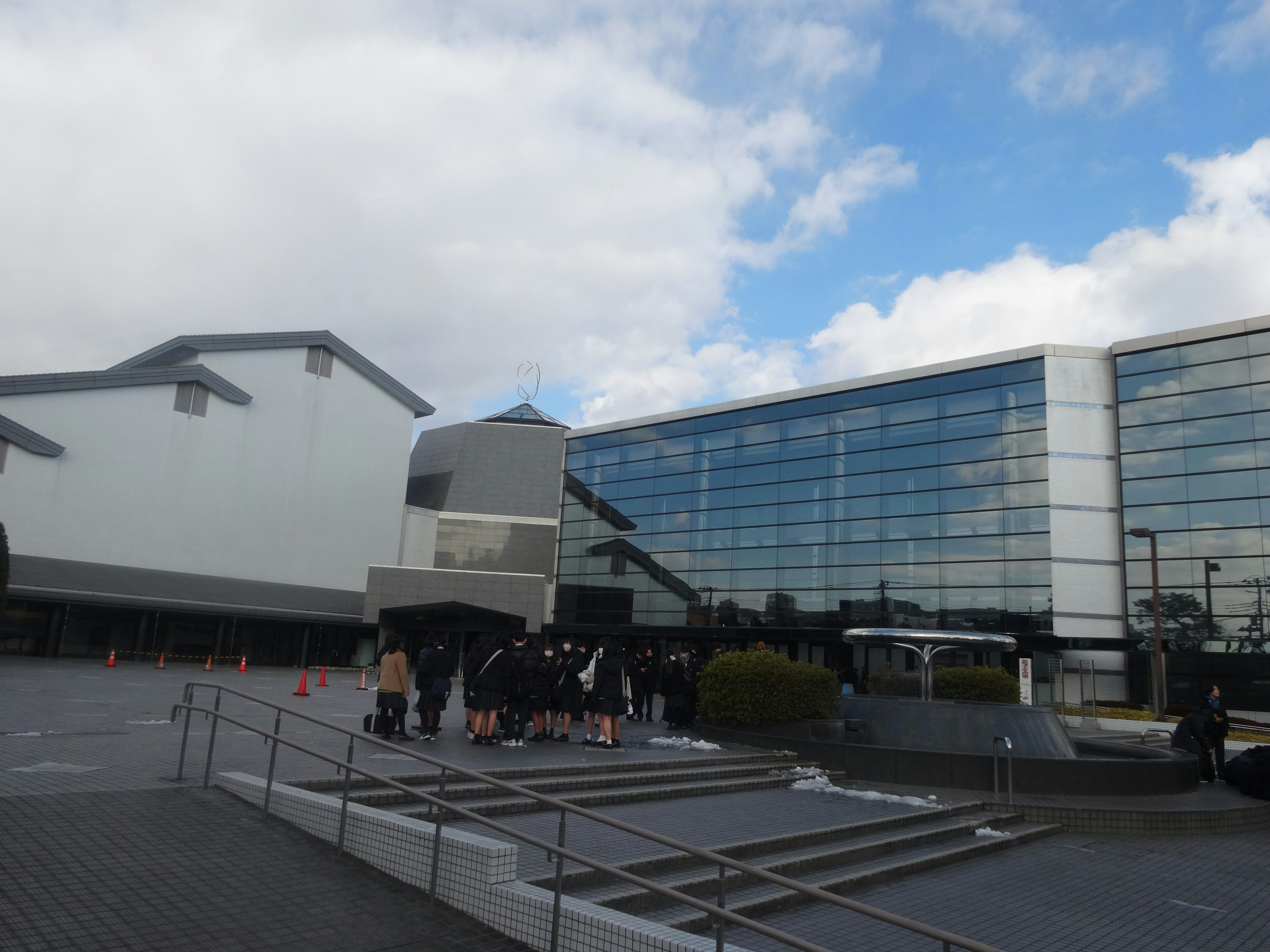 People gathered in front of a facility with a white exterior and glass facade