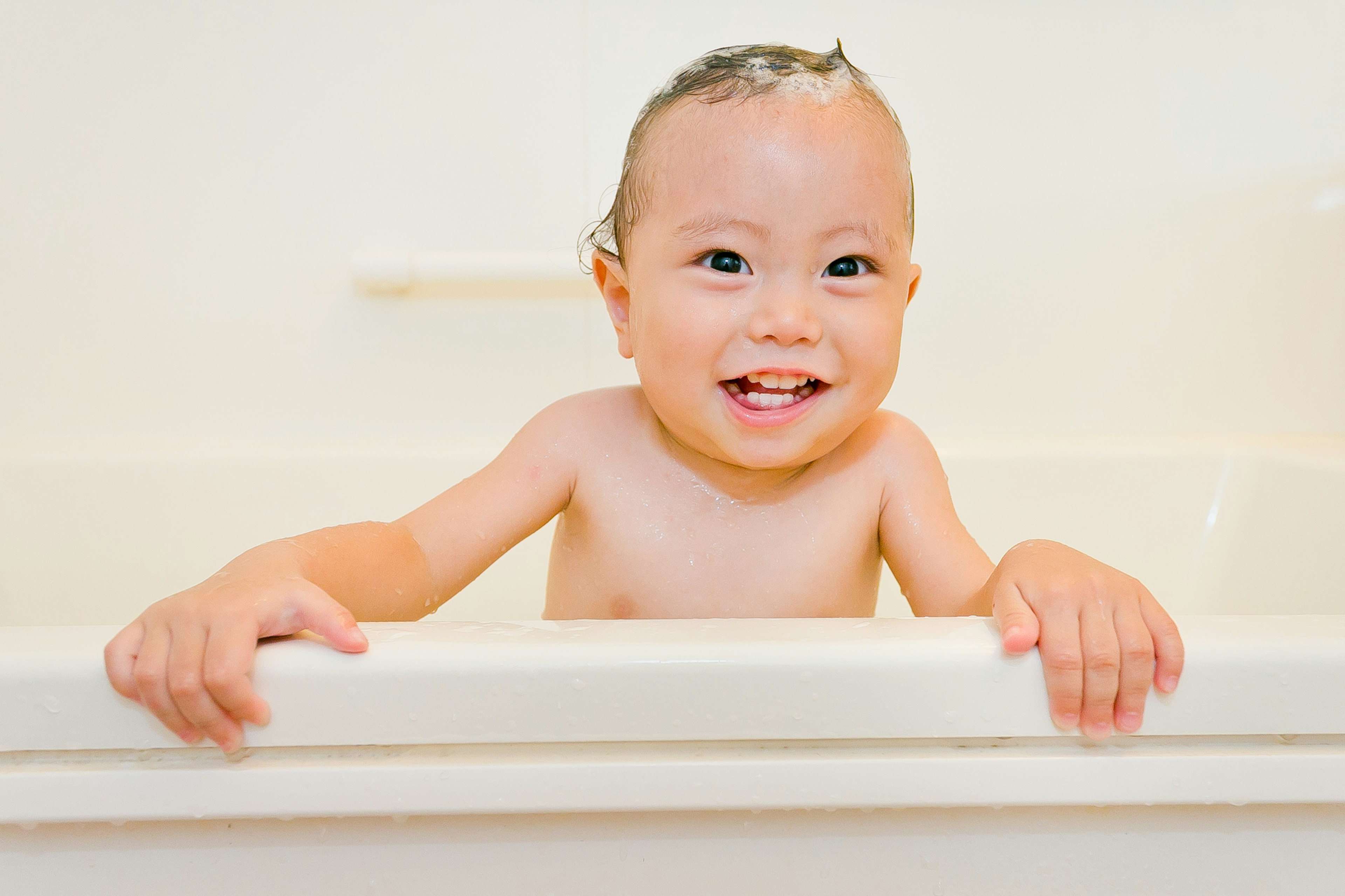 Seorang bayi tersenyum sambil memegang tepi bak mandi