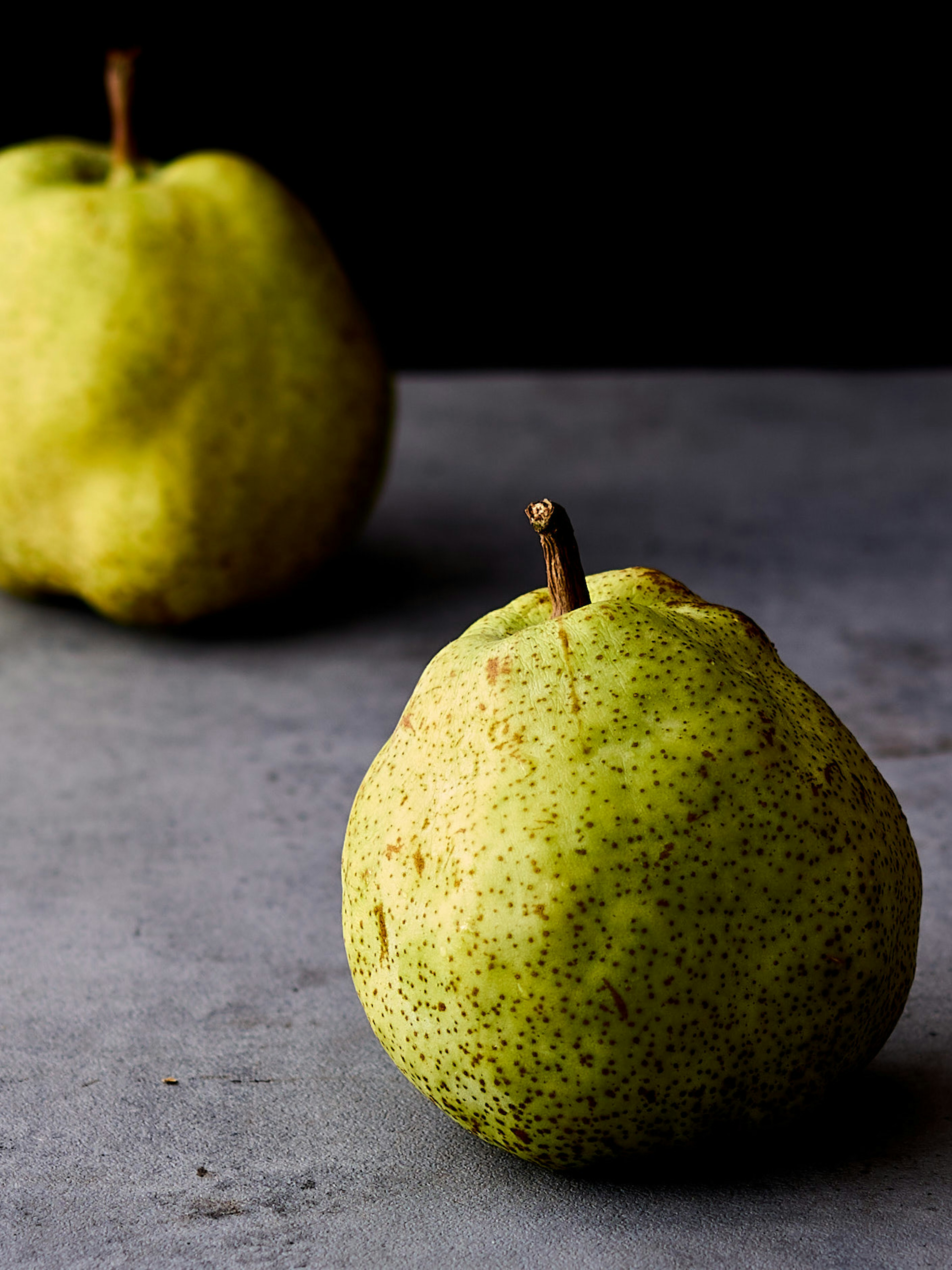 Two green pears on a dark background with a textured surface