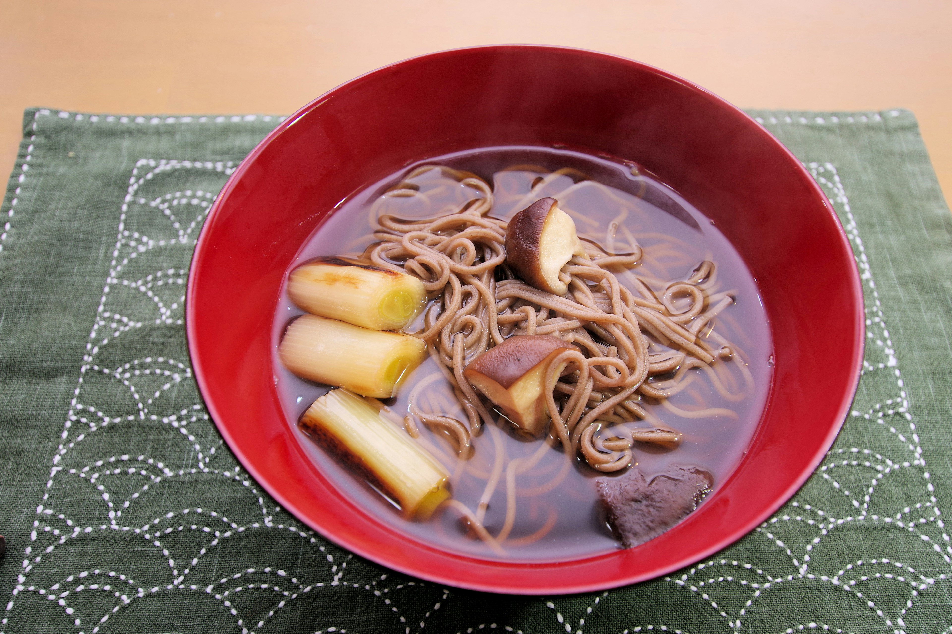 Soba noodles in a red bowl with leeks and broth