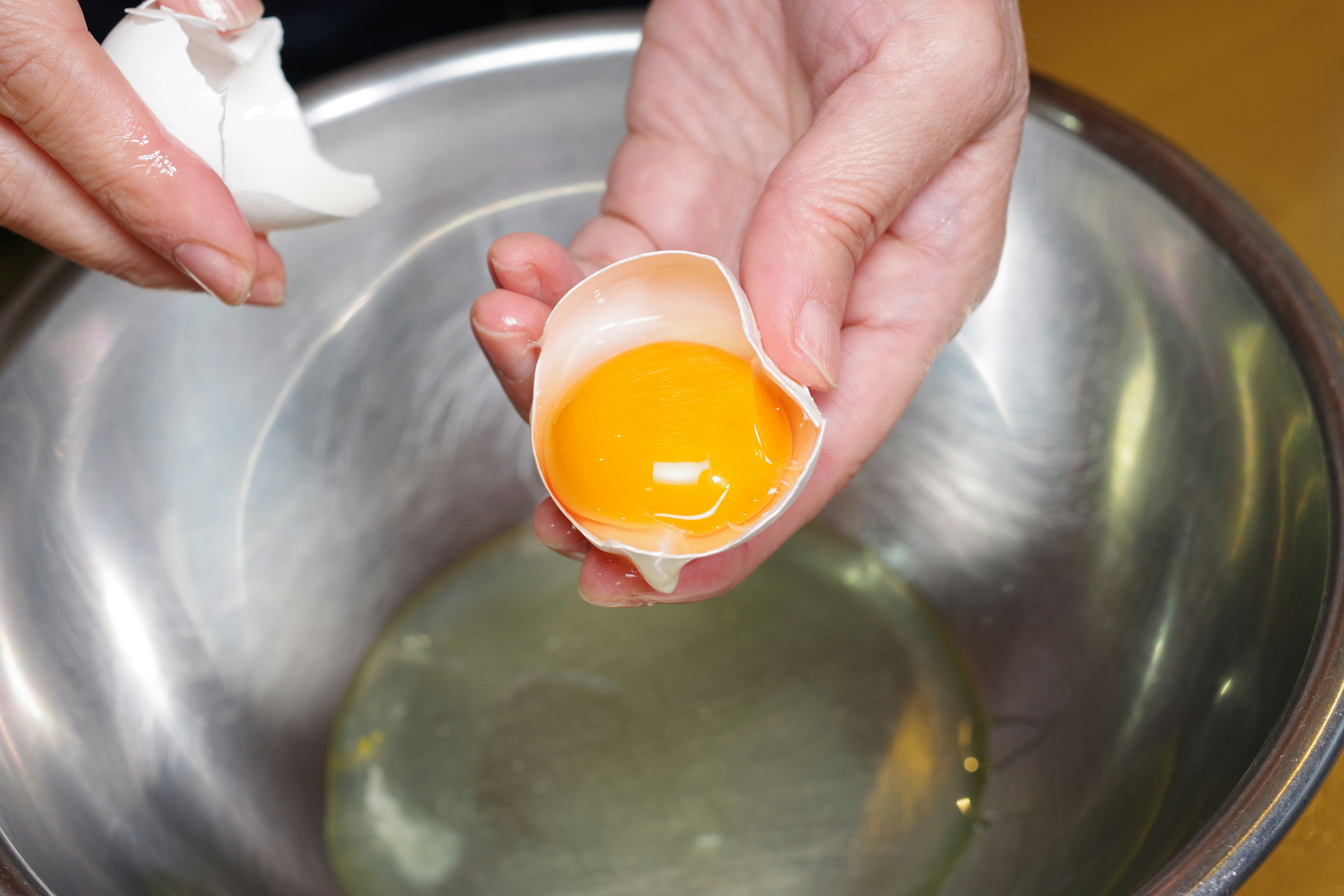 Mains cassant un œuf et versant le jaune dans un bol