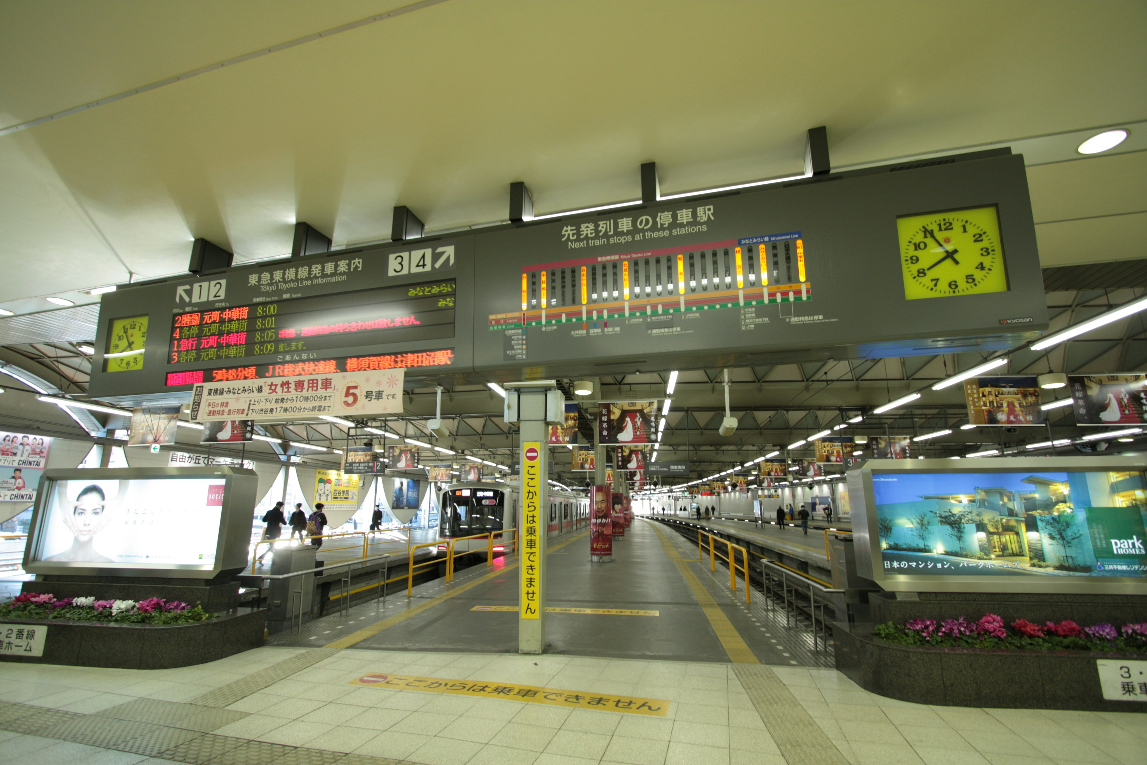 View of a train station platform featuring a schedule board and advertisements