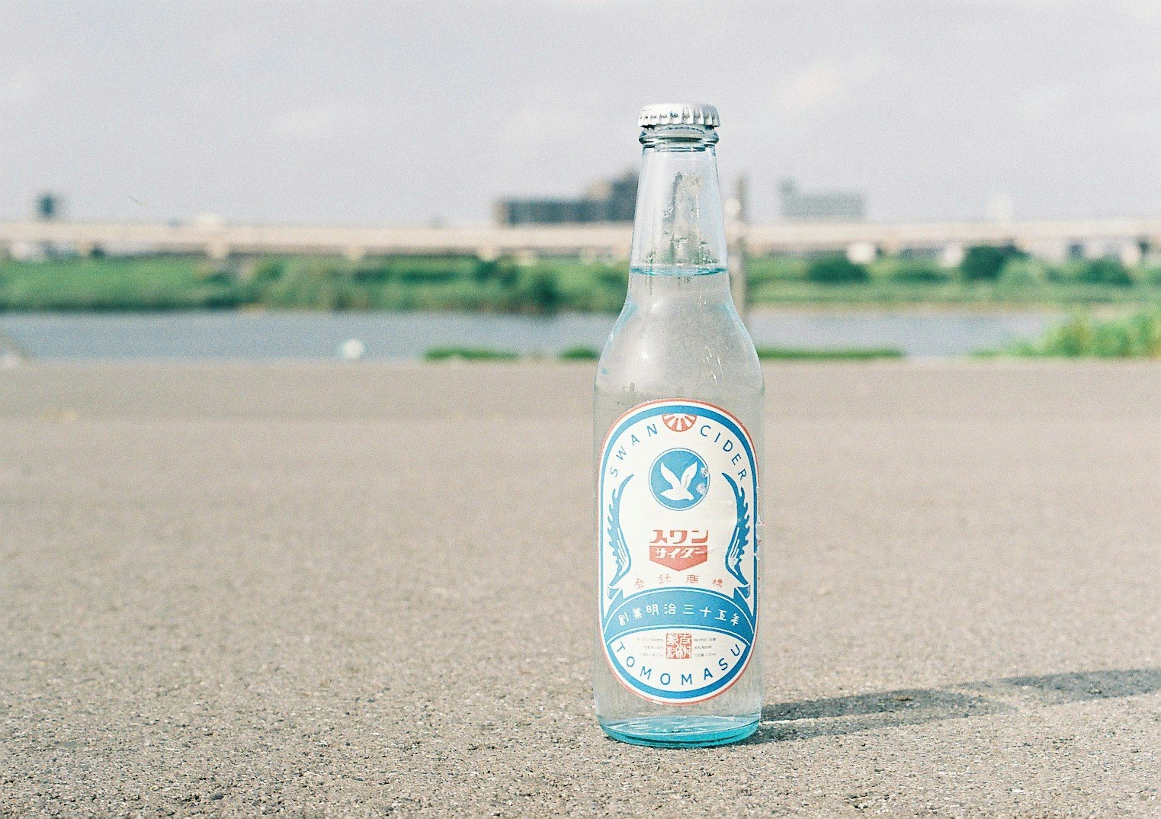 A glass bottle of a blue-labeled beverage placed near a river