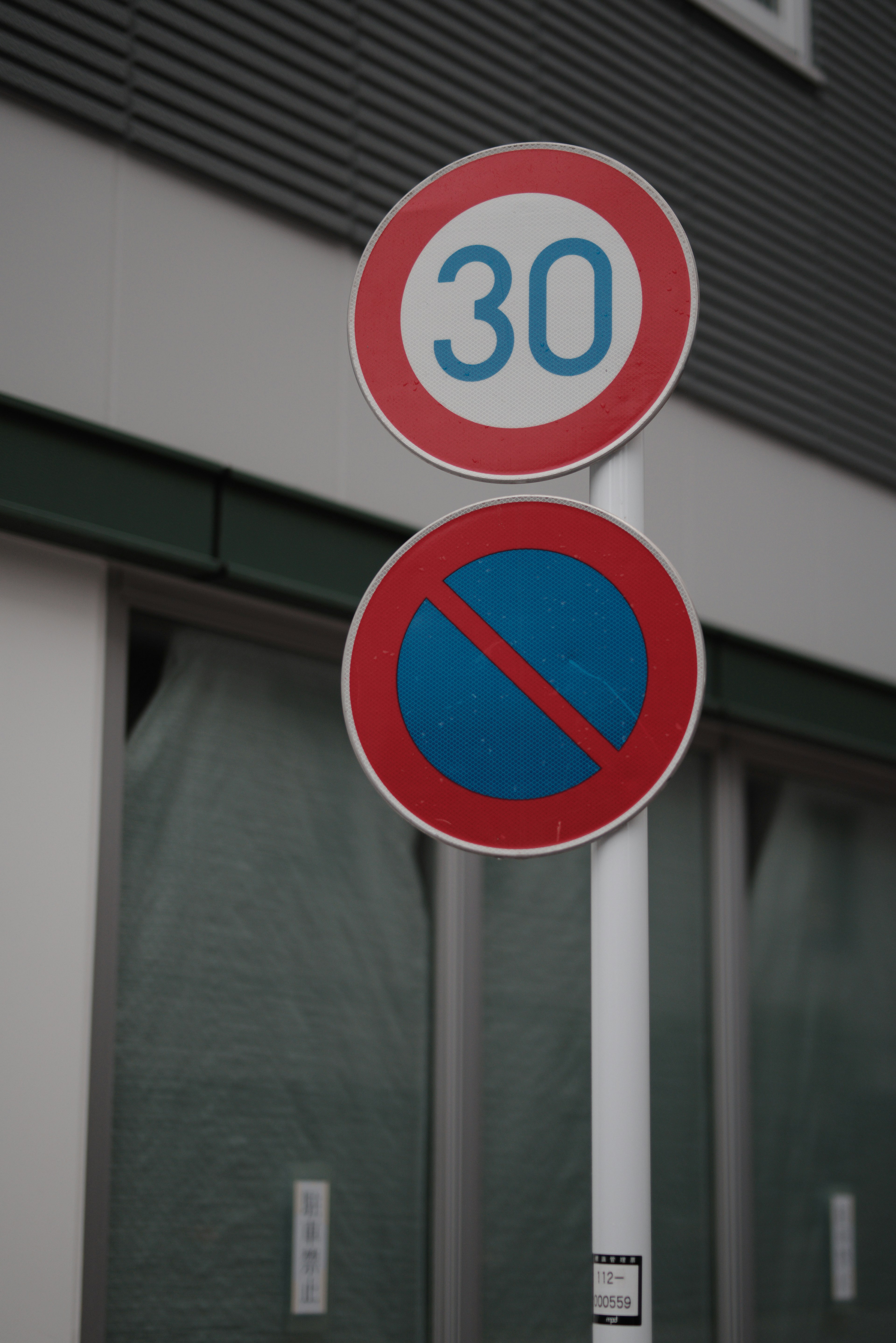 A red circular sign with a speed limit of 30 and a blue no parking sign below it