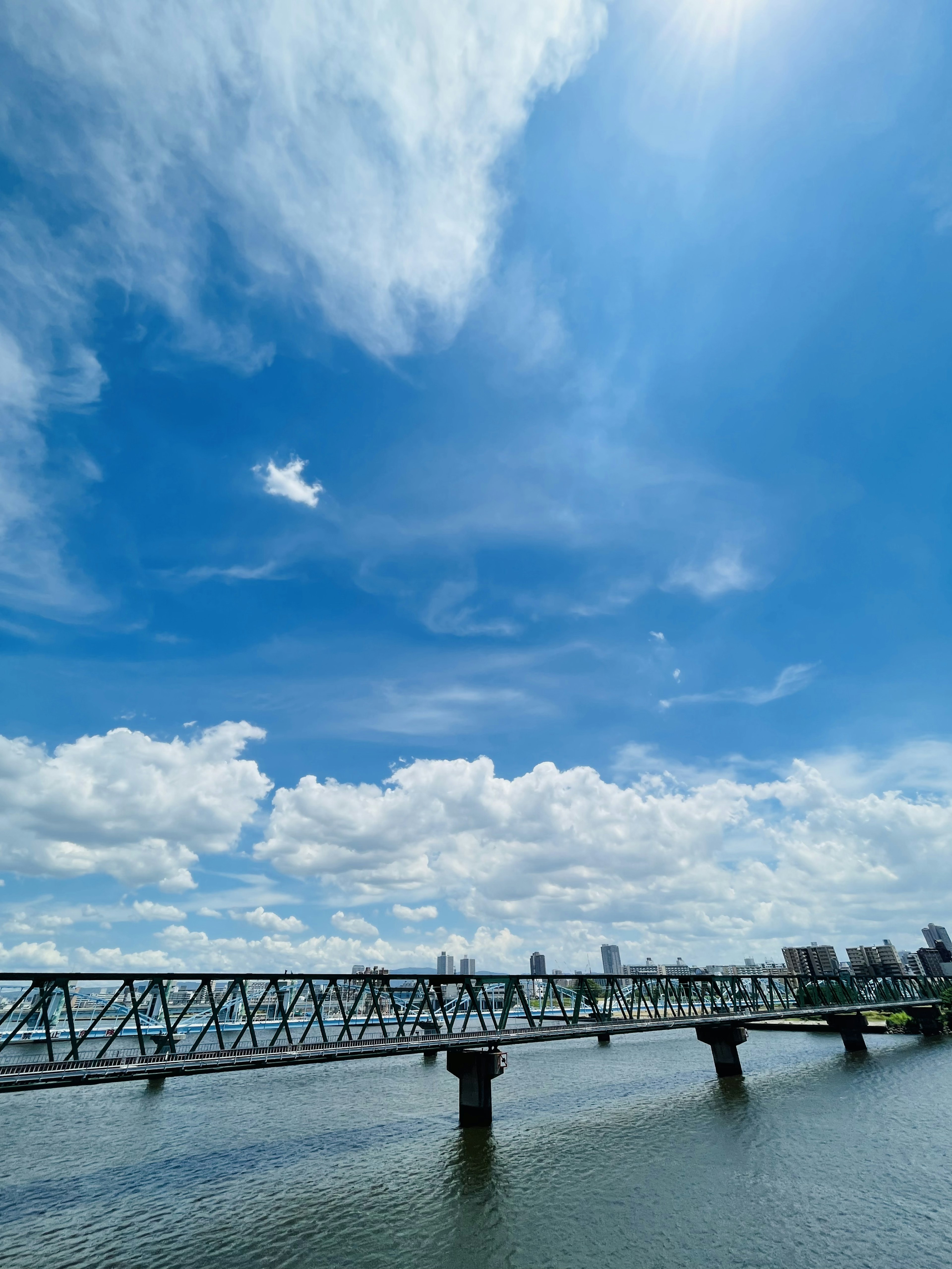 Una vista di un ponte in acciaio che si estende sopra l'acqua sotto un cielo blu luminoso con nuvole