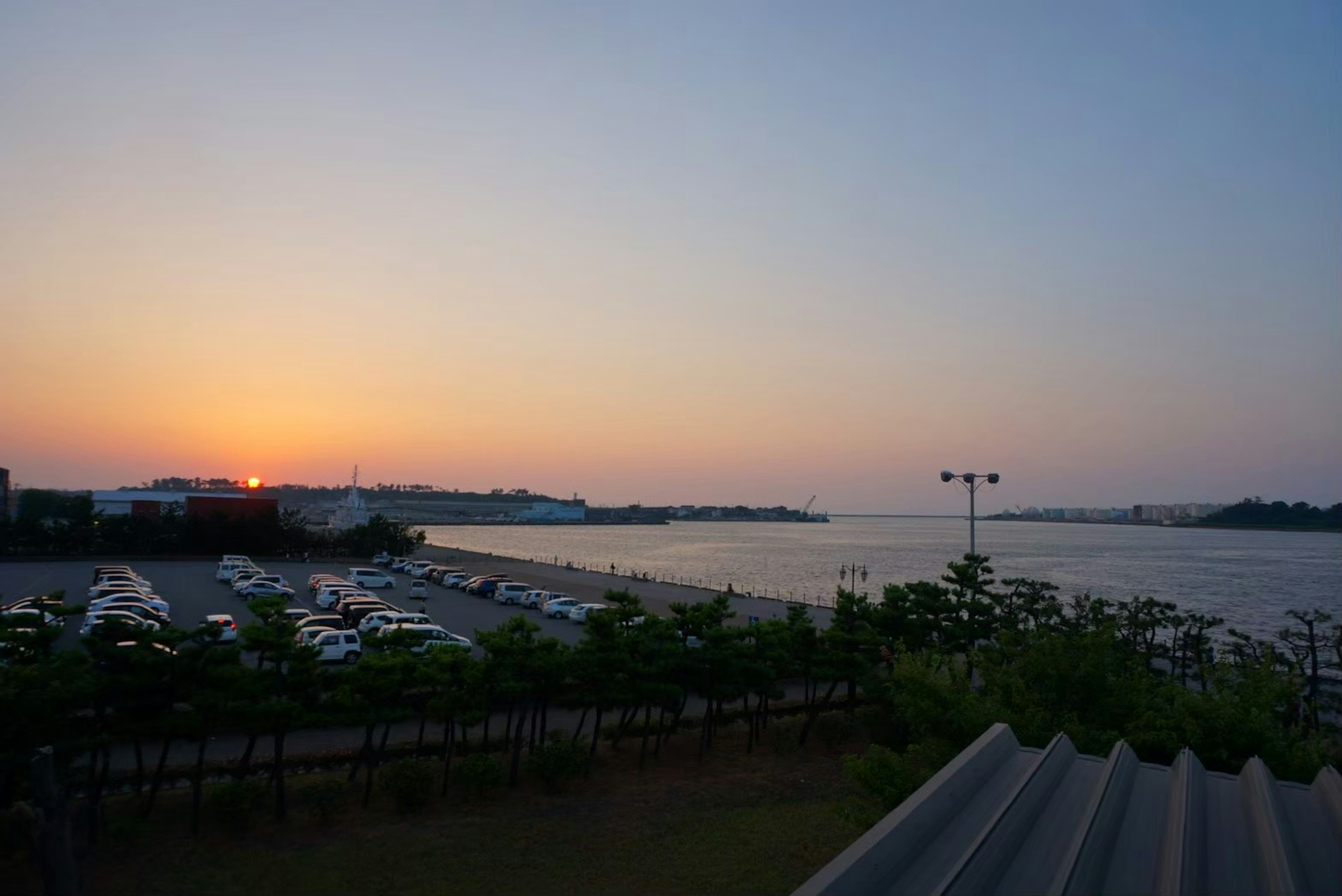 Vue pittoresque d'un coucher de soleil sur l'eau avec un parking et des arbres