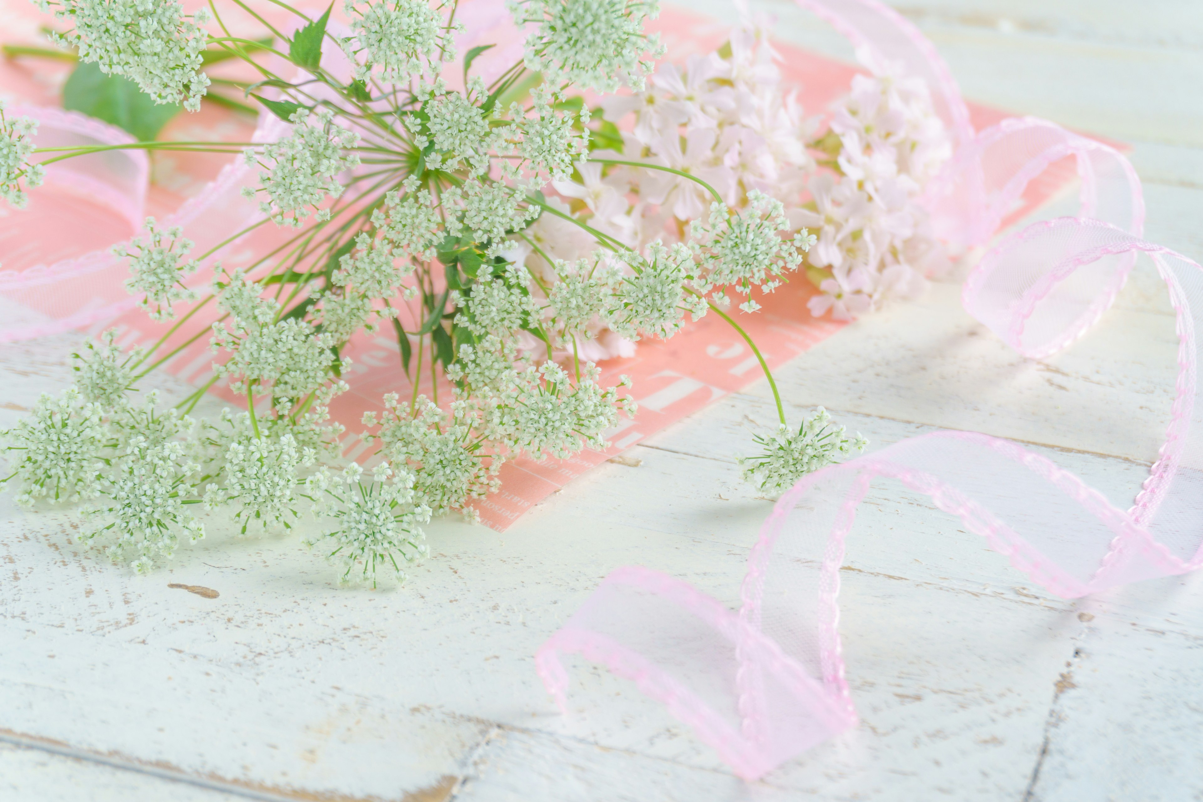 A bouquet of flowers with pale pink ribbon on a wooden table