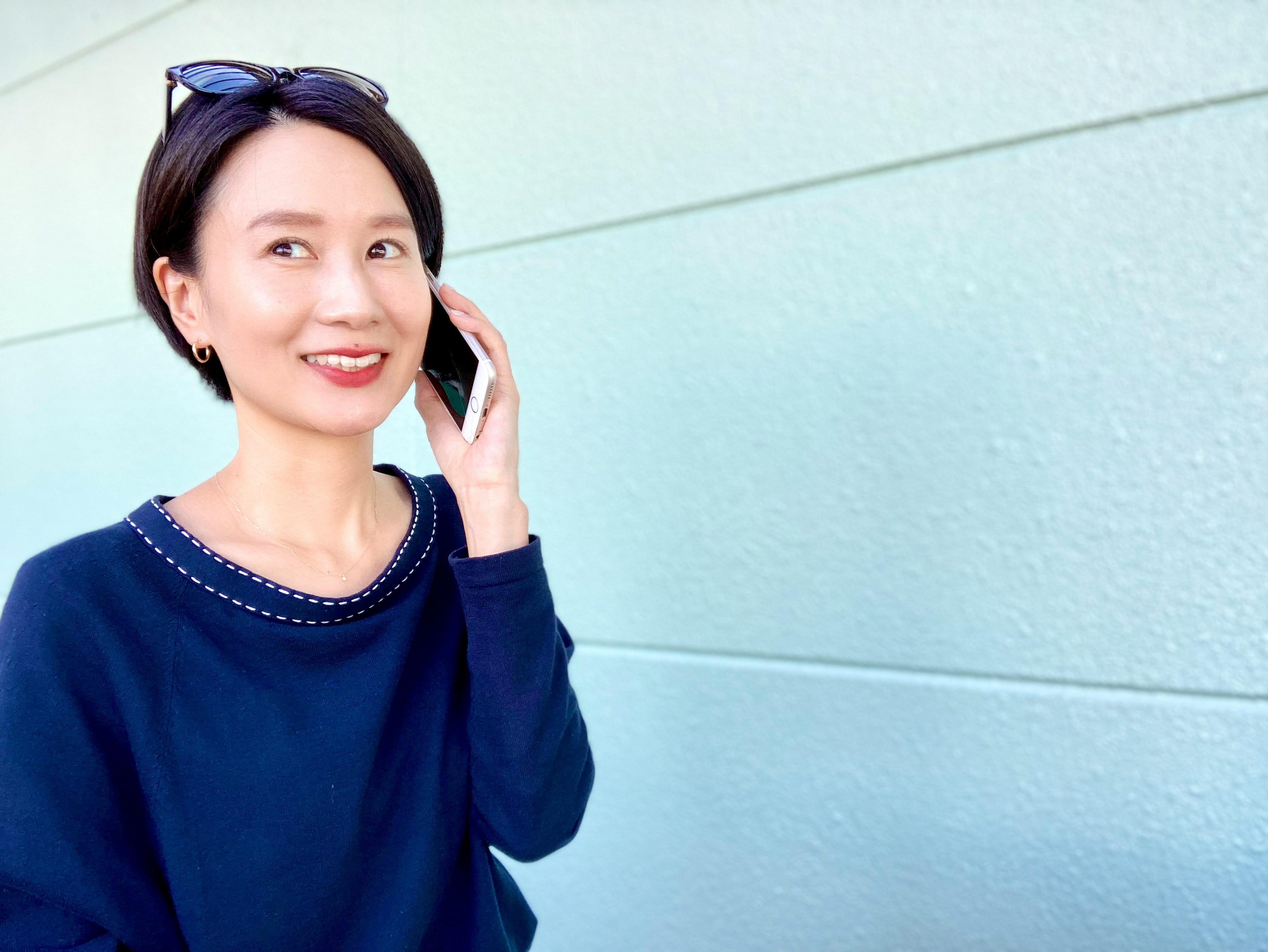 A woman smiling while talking on the phone against a light blue wall