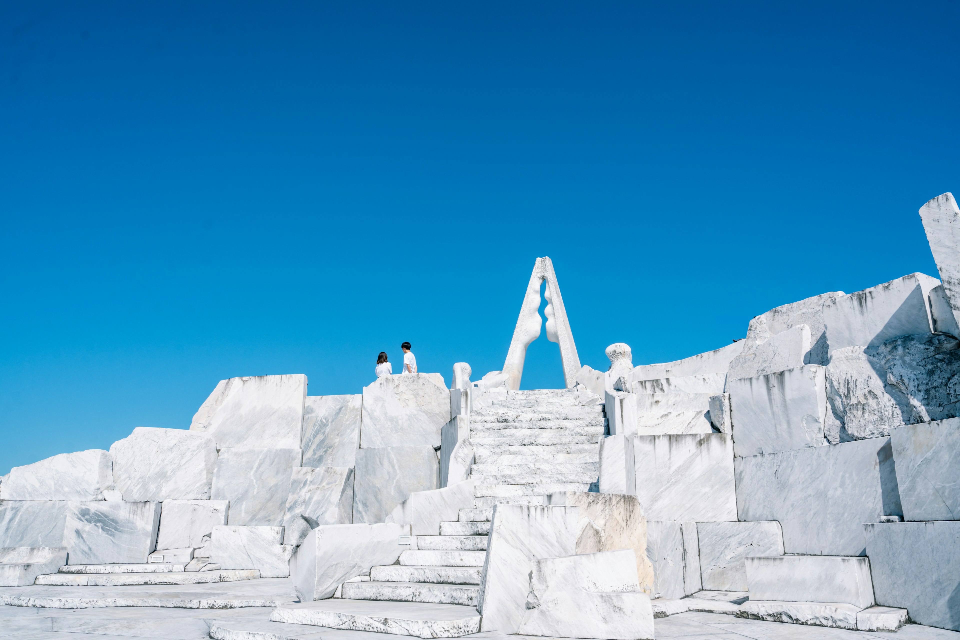 White marble ruins under a clear blue sky with two figures