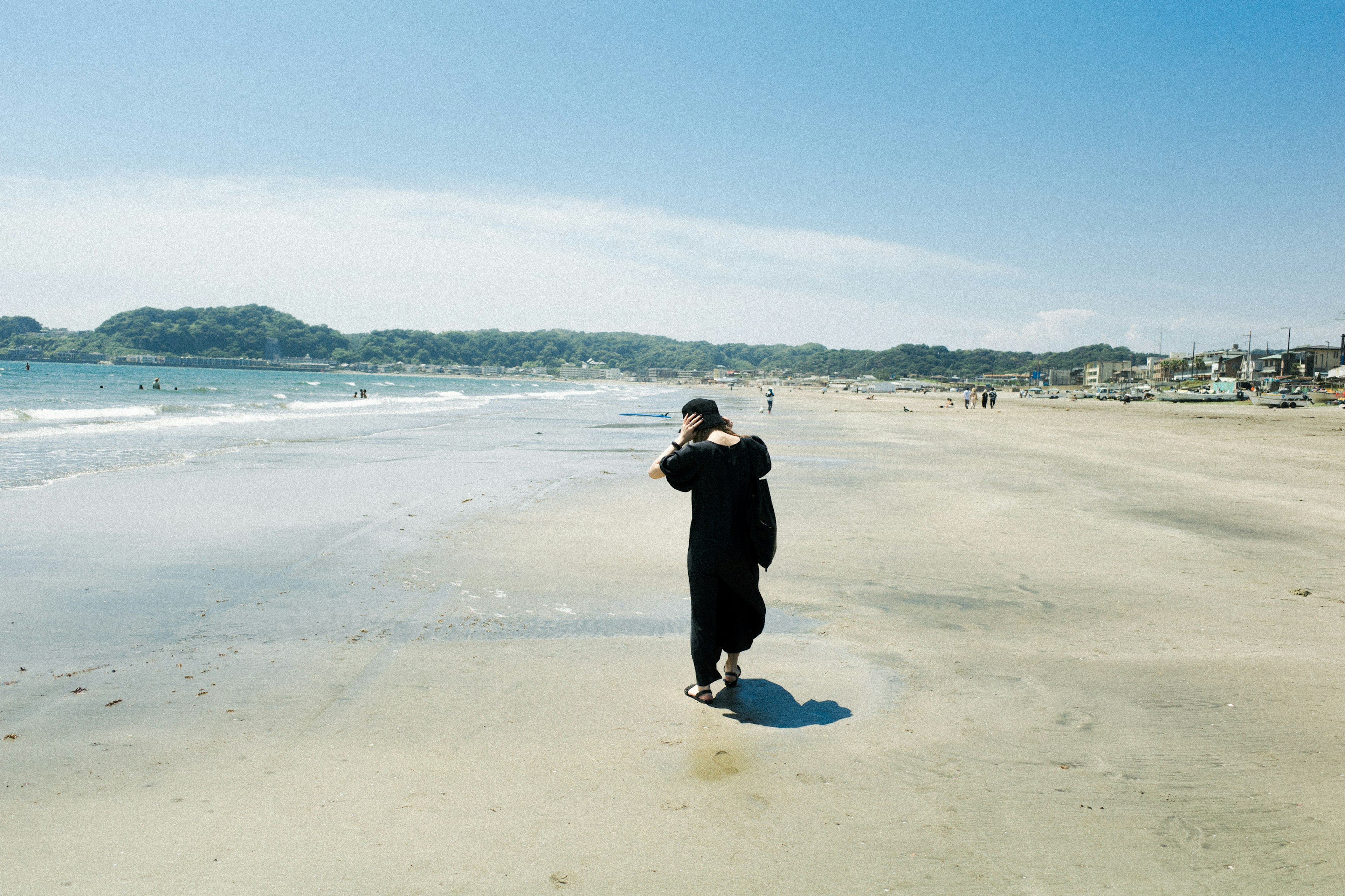 海辺を歩く黒い服の人物と青い空