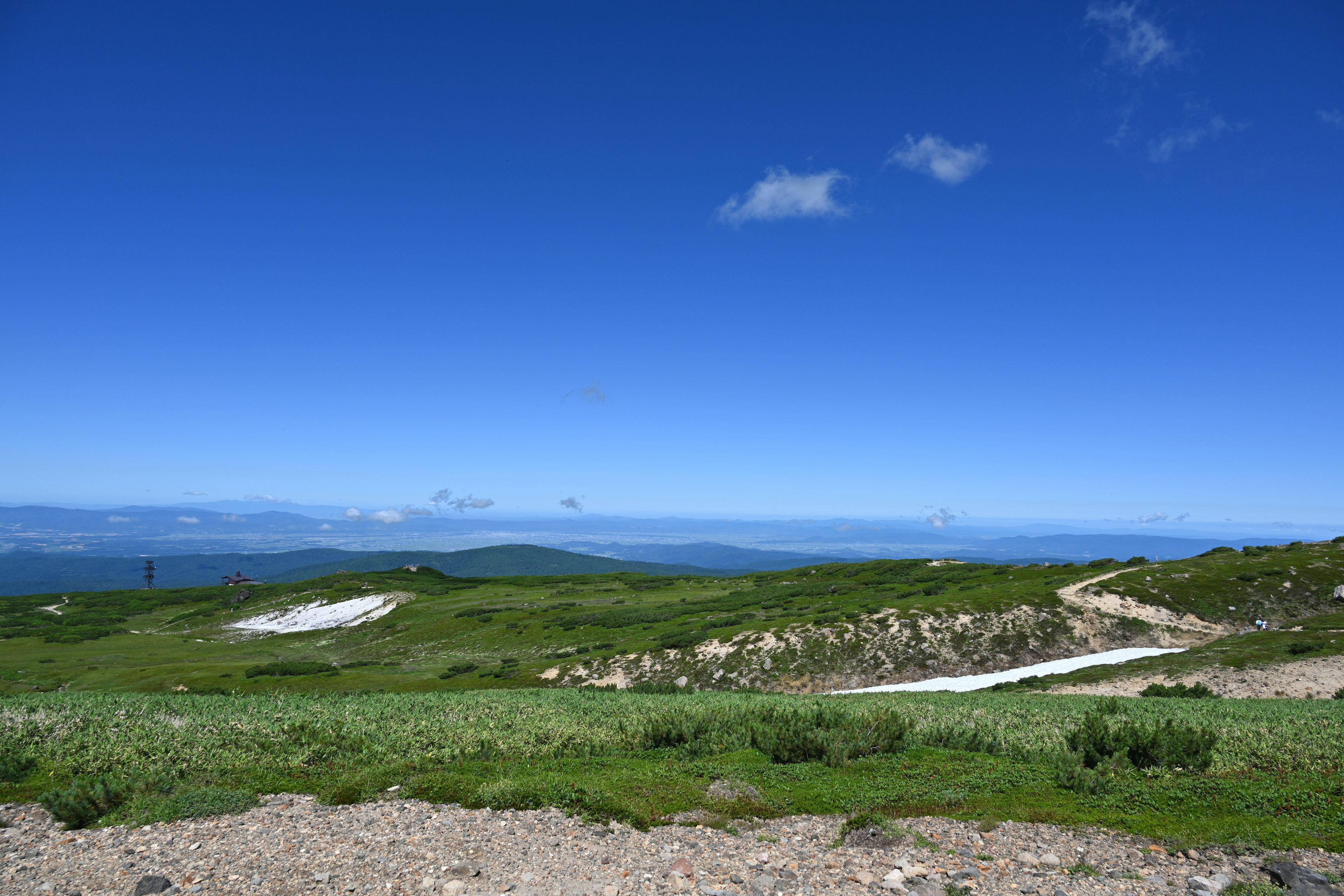 Landschaft mit klarem blauen Himmel und sanften grünen Hügeln mit entfernten Bergen