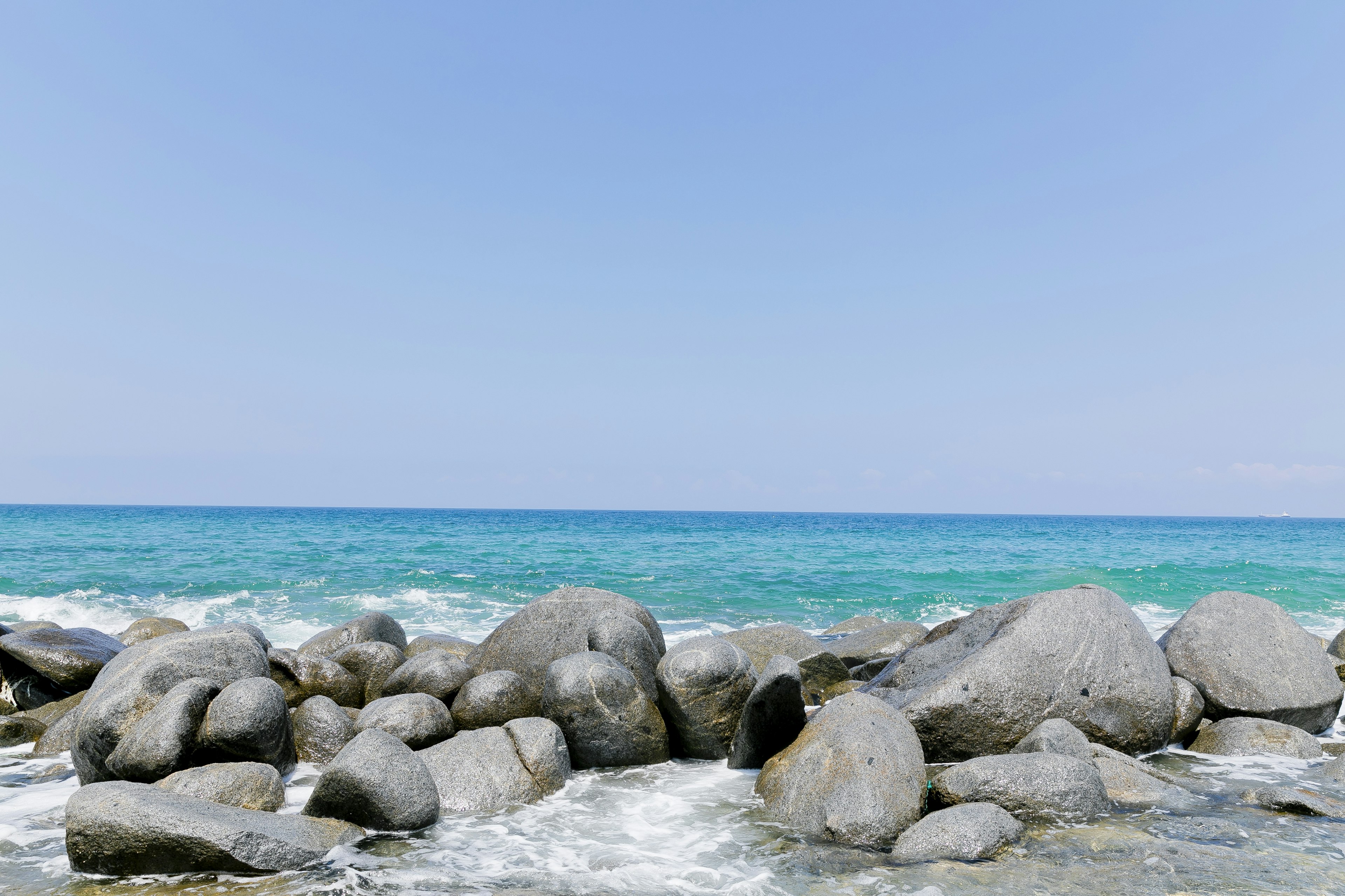 Large rocks by a tranquil blue sea under a clear sky