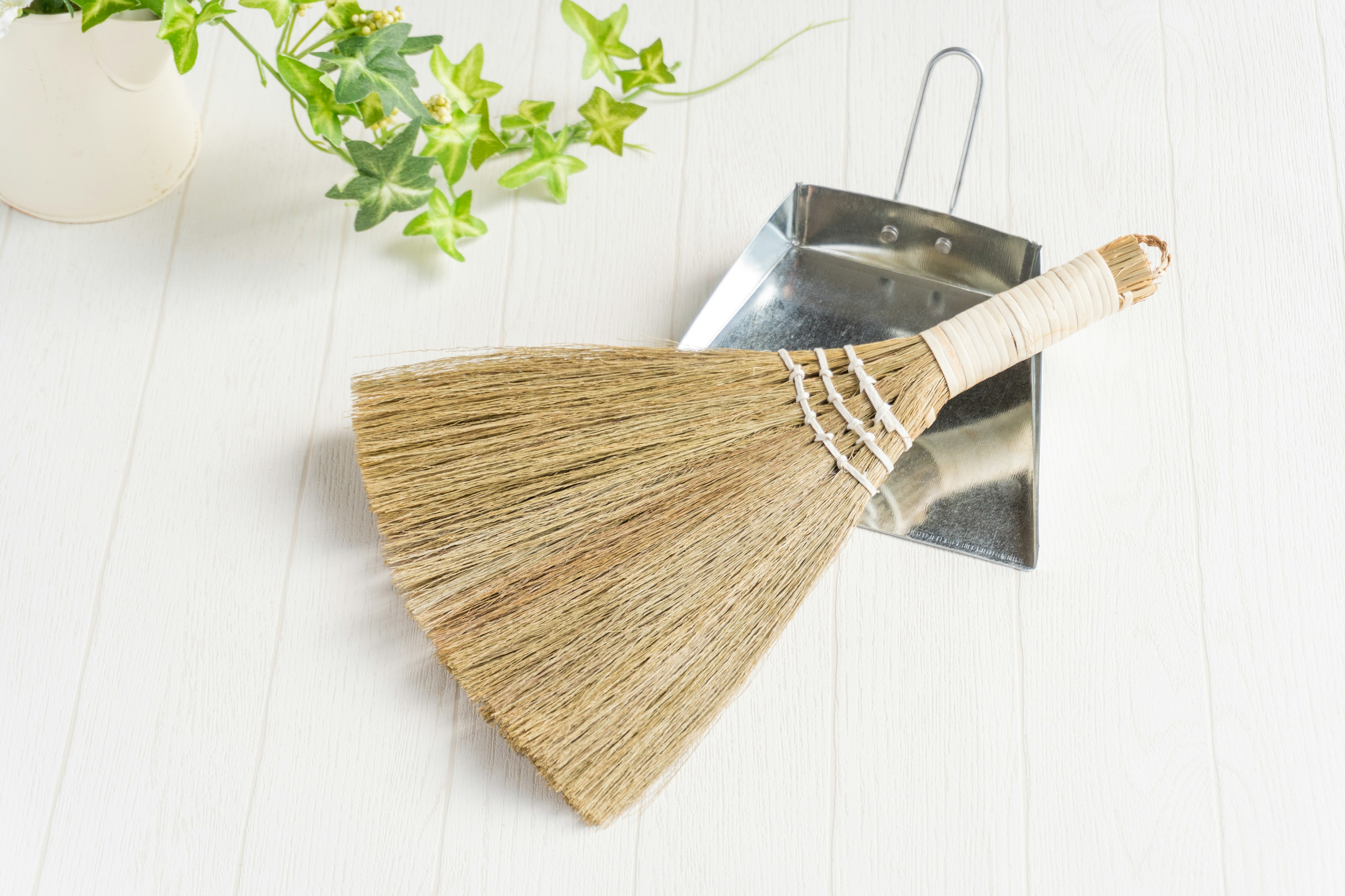 un balai et une pelle à poussière posés sur une table blanche à côté d'une plante verte