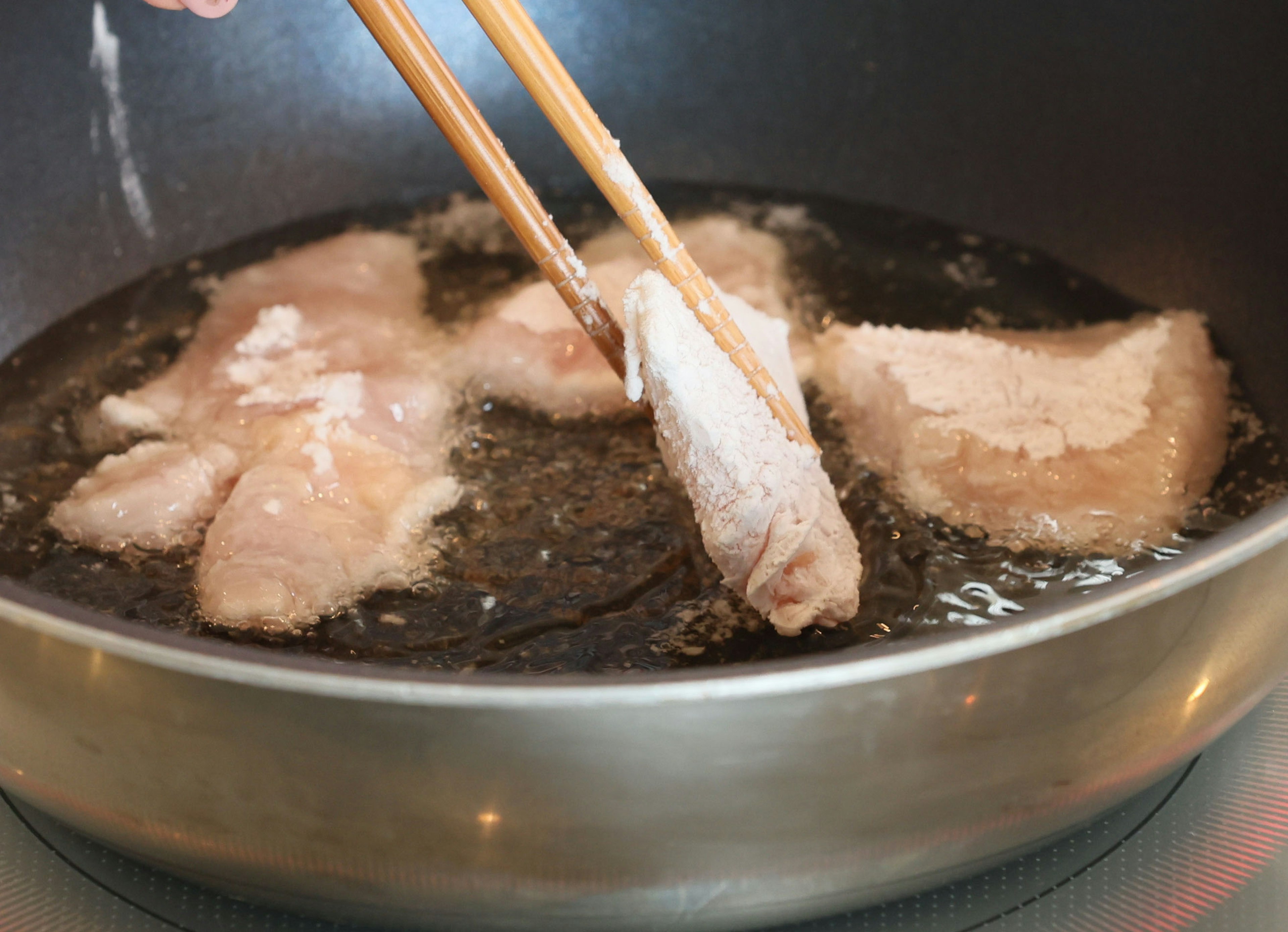 Pieces of meat frying in a pan being lifted with chopsticks