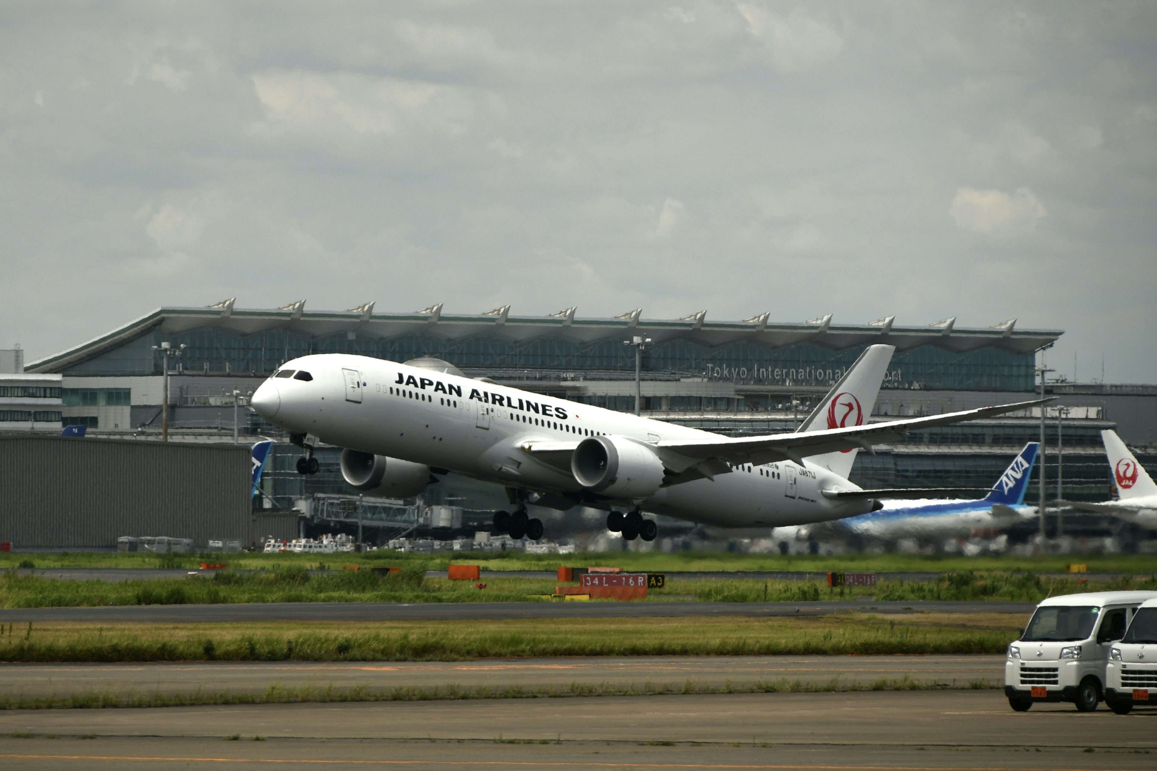 Japan Airlines Passagierflugzeug beim Start mit Flughafen im Hintergrund