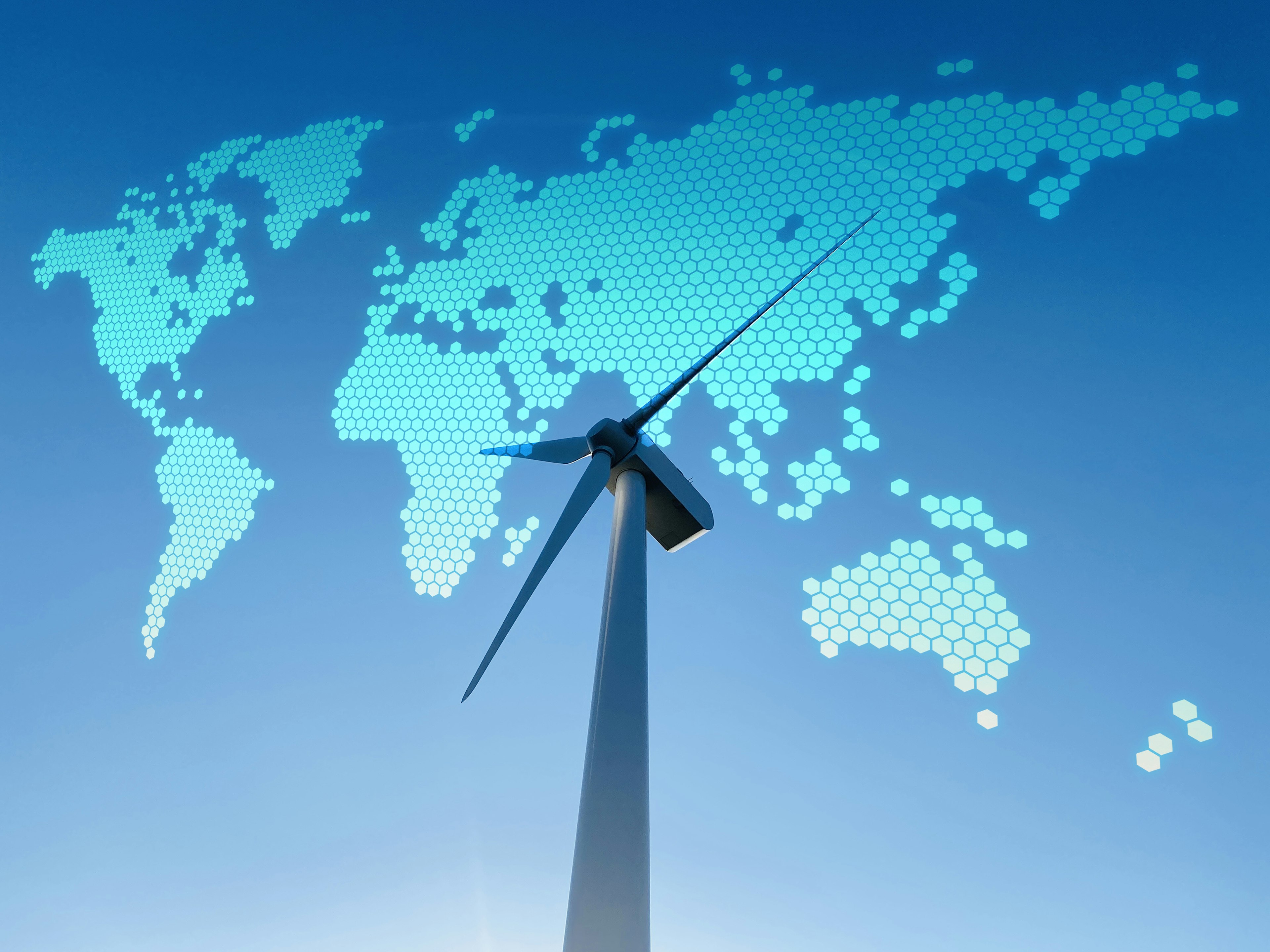 Wind turbine against blue sky with digital world map overlay