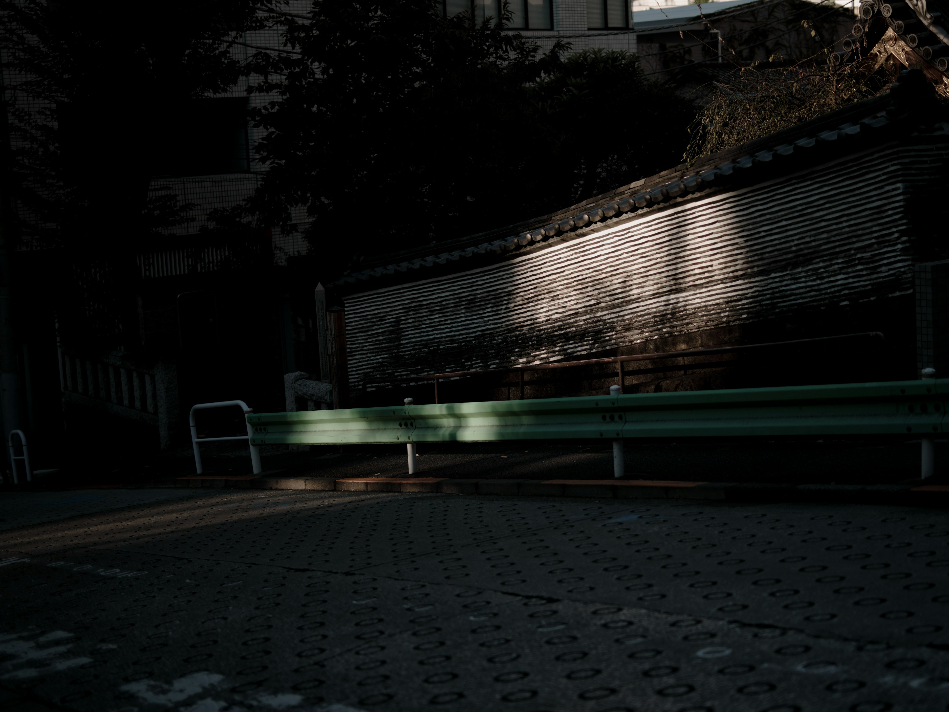 A quiet scene featuring a green bench against a dark background with part of a wall visible