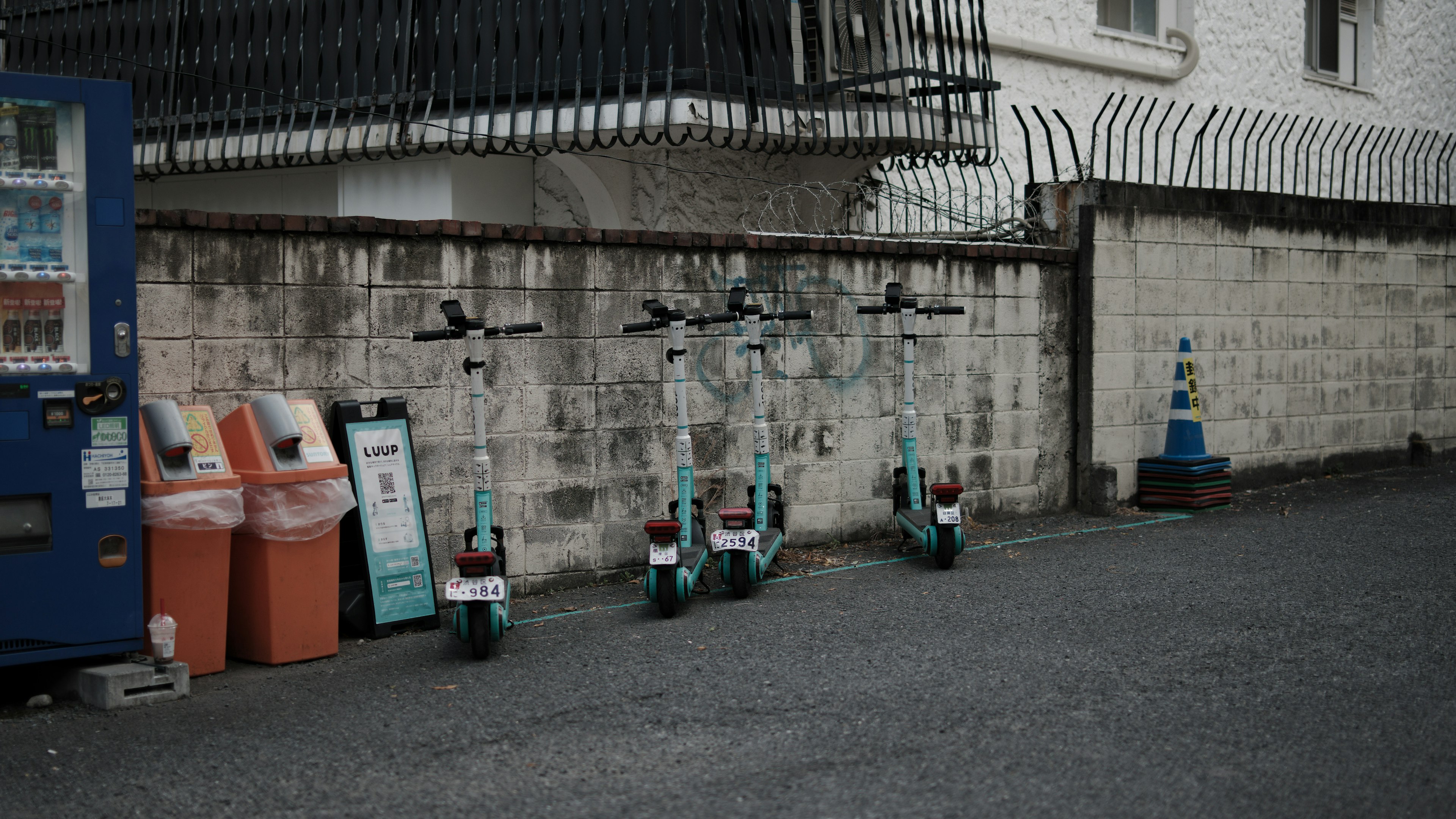 Image of electric scooters lined against a wall with trash bins