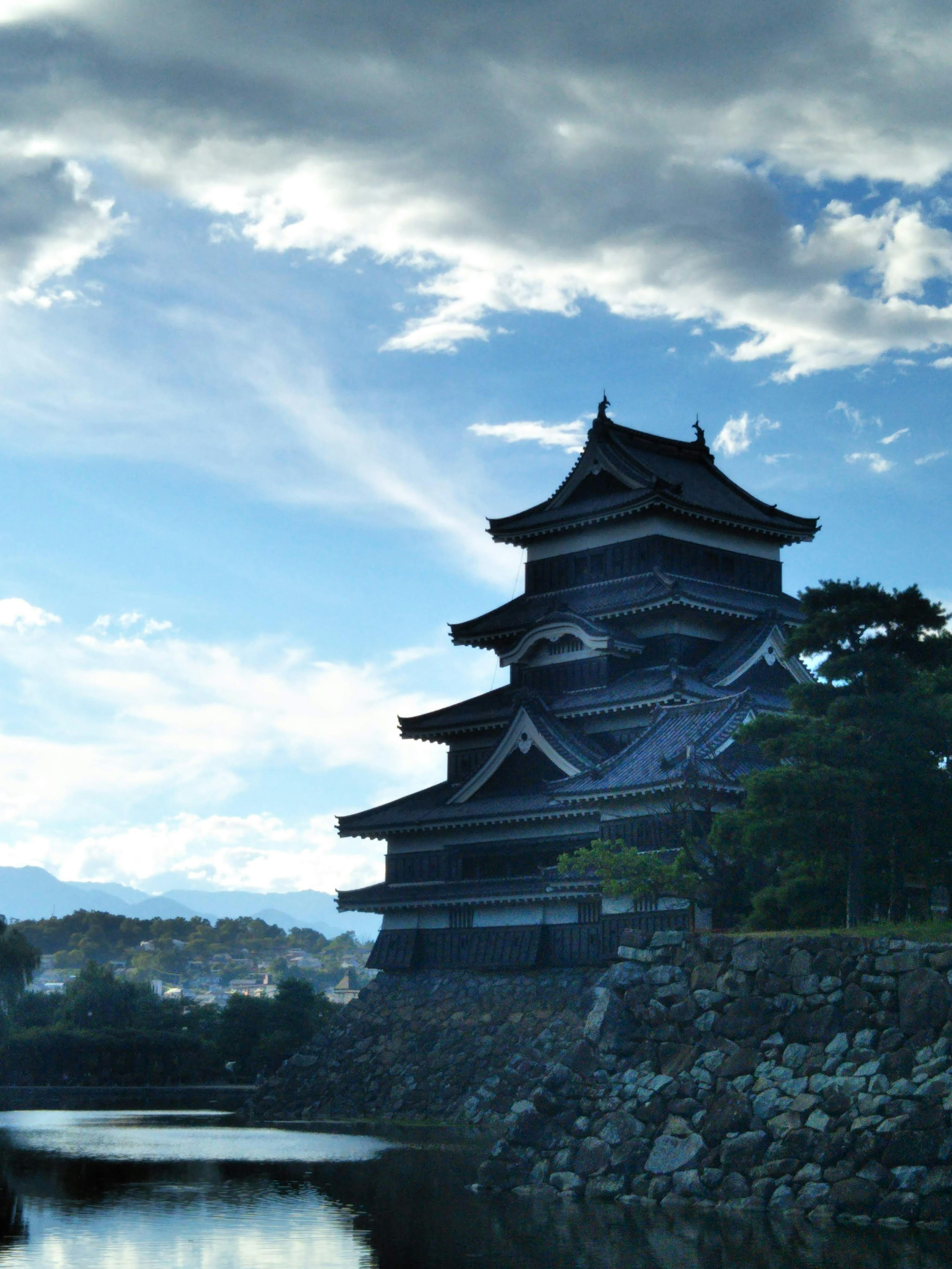 Silhouette of Matsumoto Castle against a blue sky and clouds