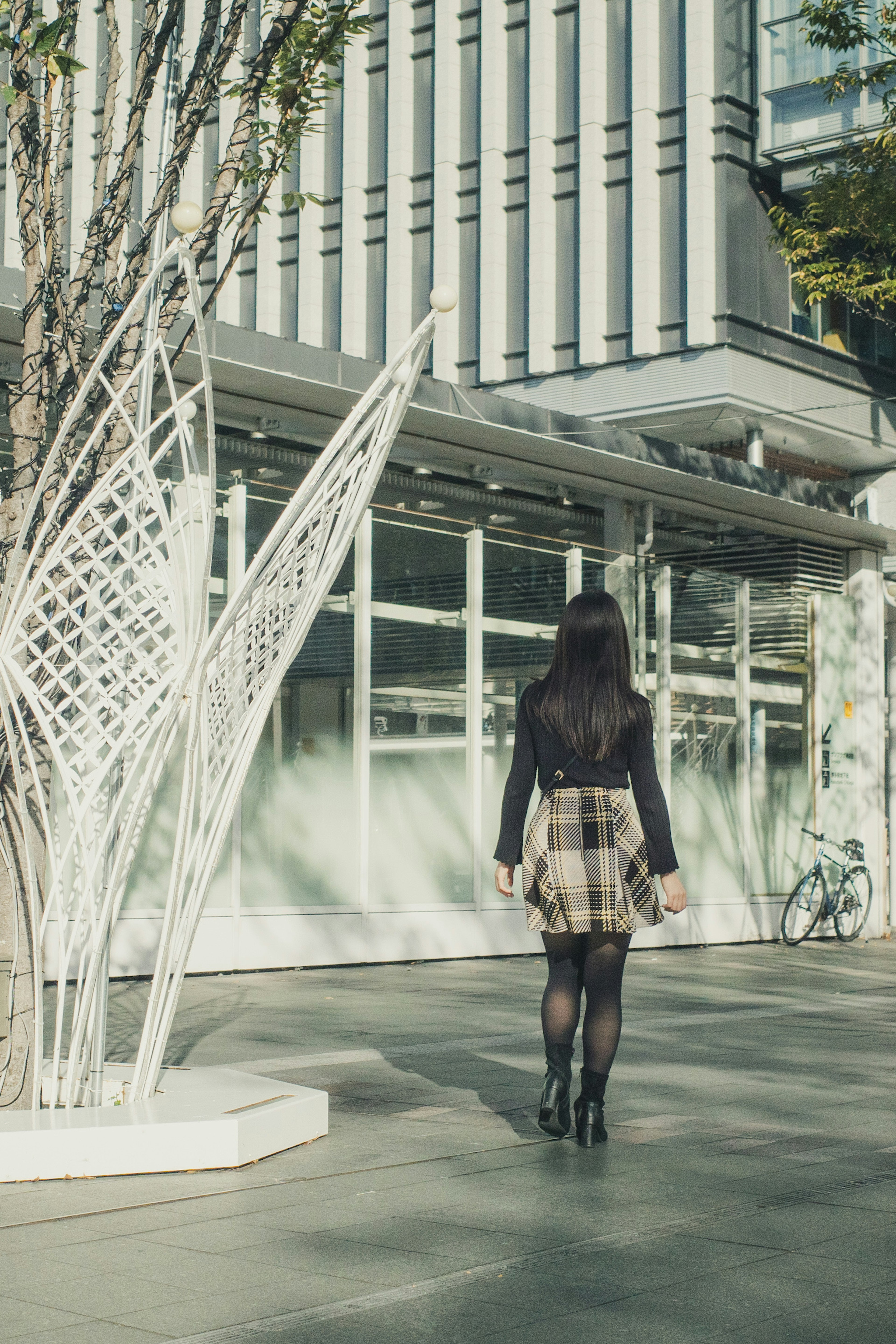 Una donna con una gonna a quadri sta con le spalle a un edificio moderno