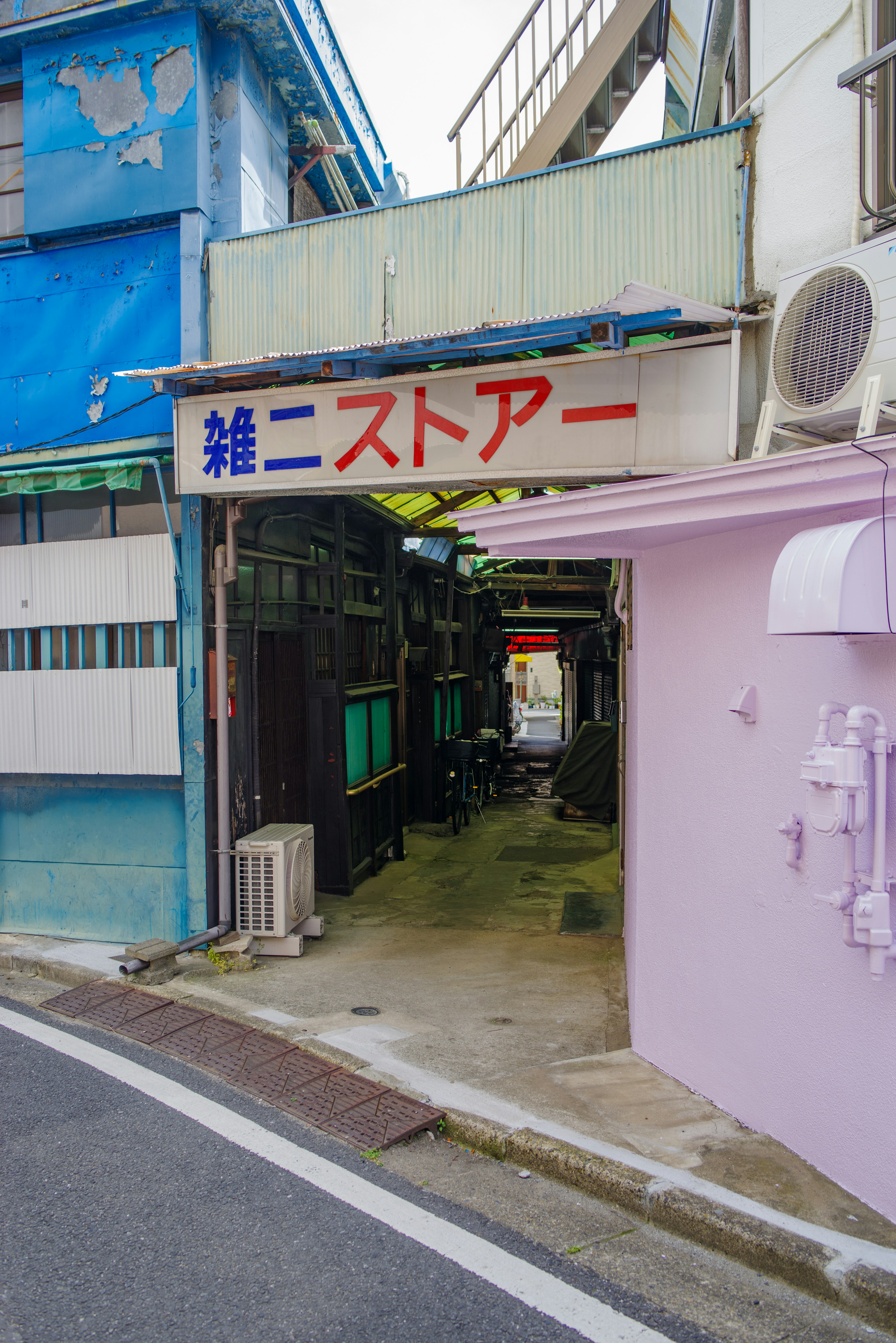 Entrance of a small shop in a narrow street with blue buildings and a pink wall