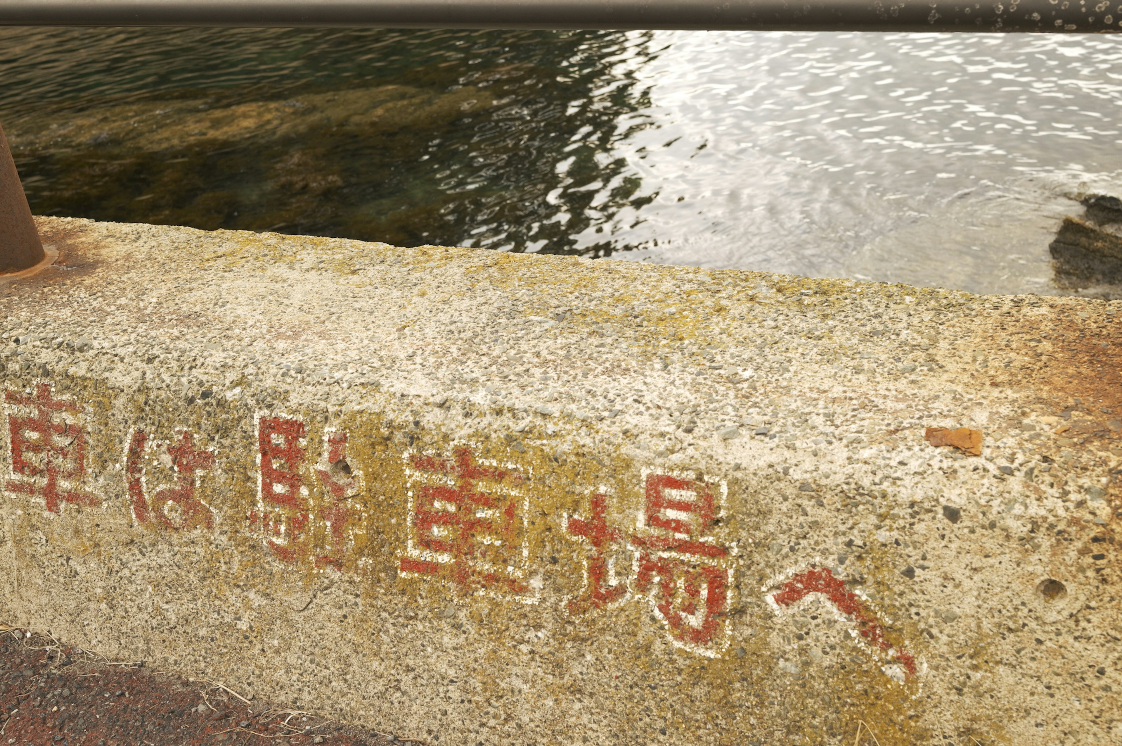 Señal en japonés en una pared de concreto cerca del agua indicando que los coches van al estacionamiento