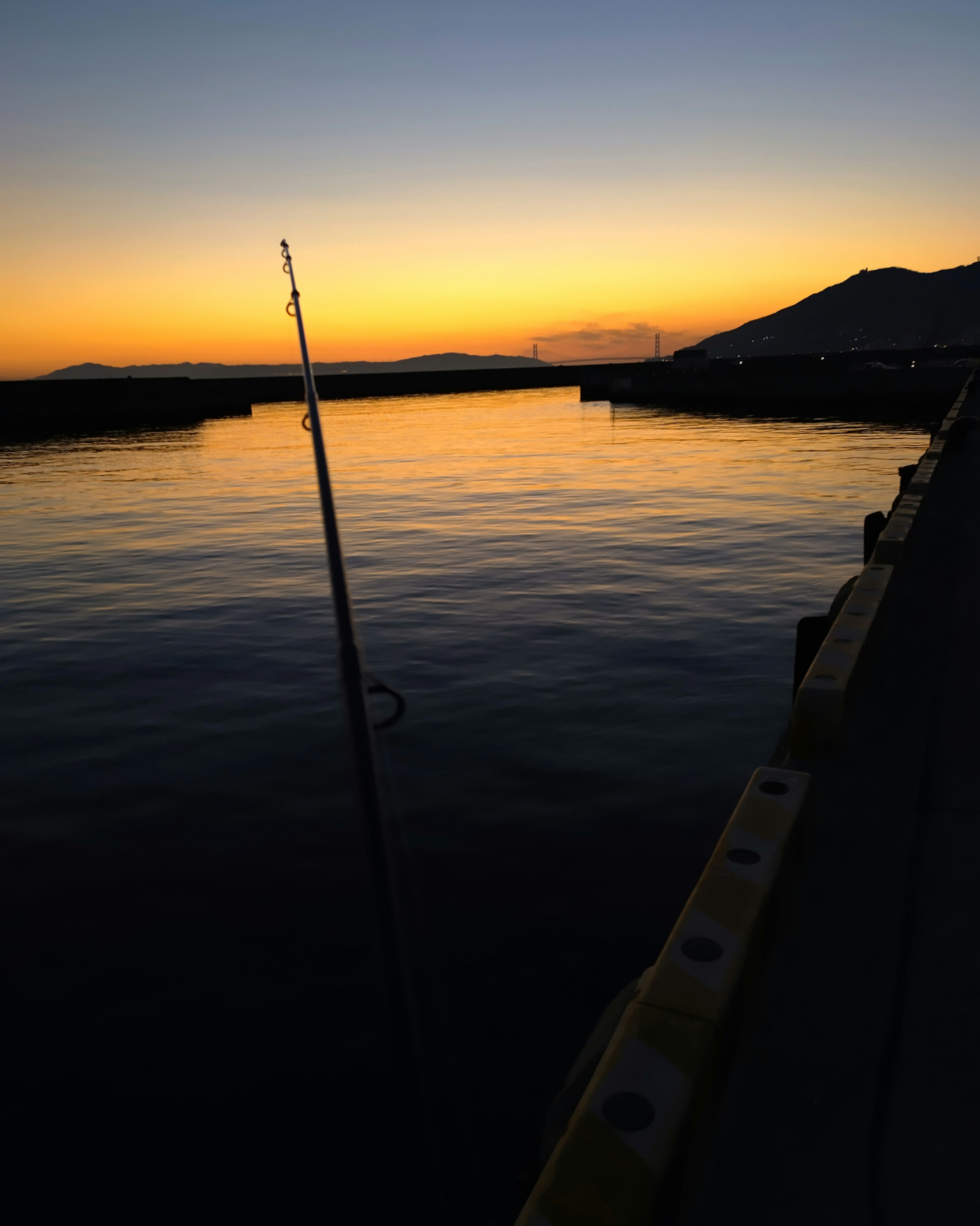 宁静的夕阳倒映在平静的水面上，视野中有一根钓鱼竿