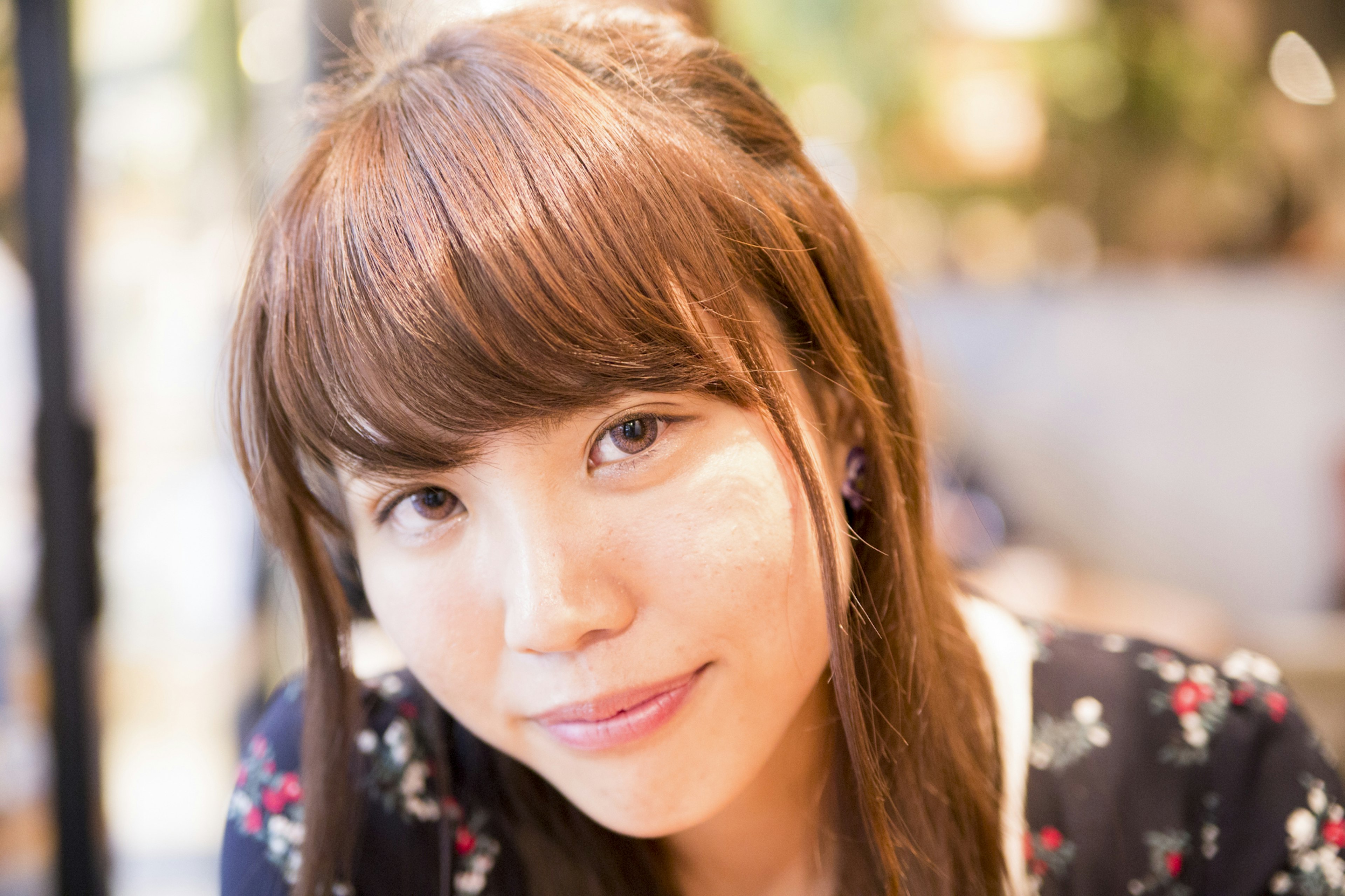 Portrait d'une femme souriante dans un café avec de longs cheveux bruns portant une robe à fleurs