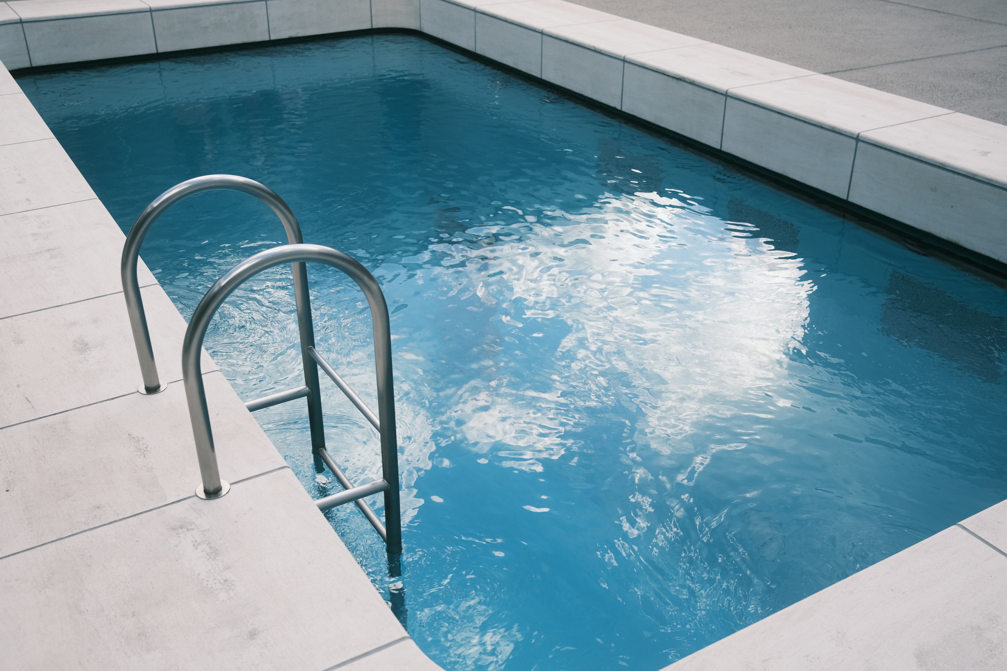 Escena al aire libre con una piscina azul y una escalera de acero inoxidable