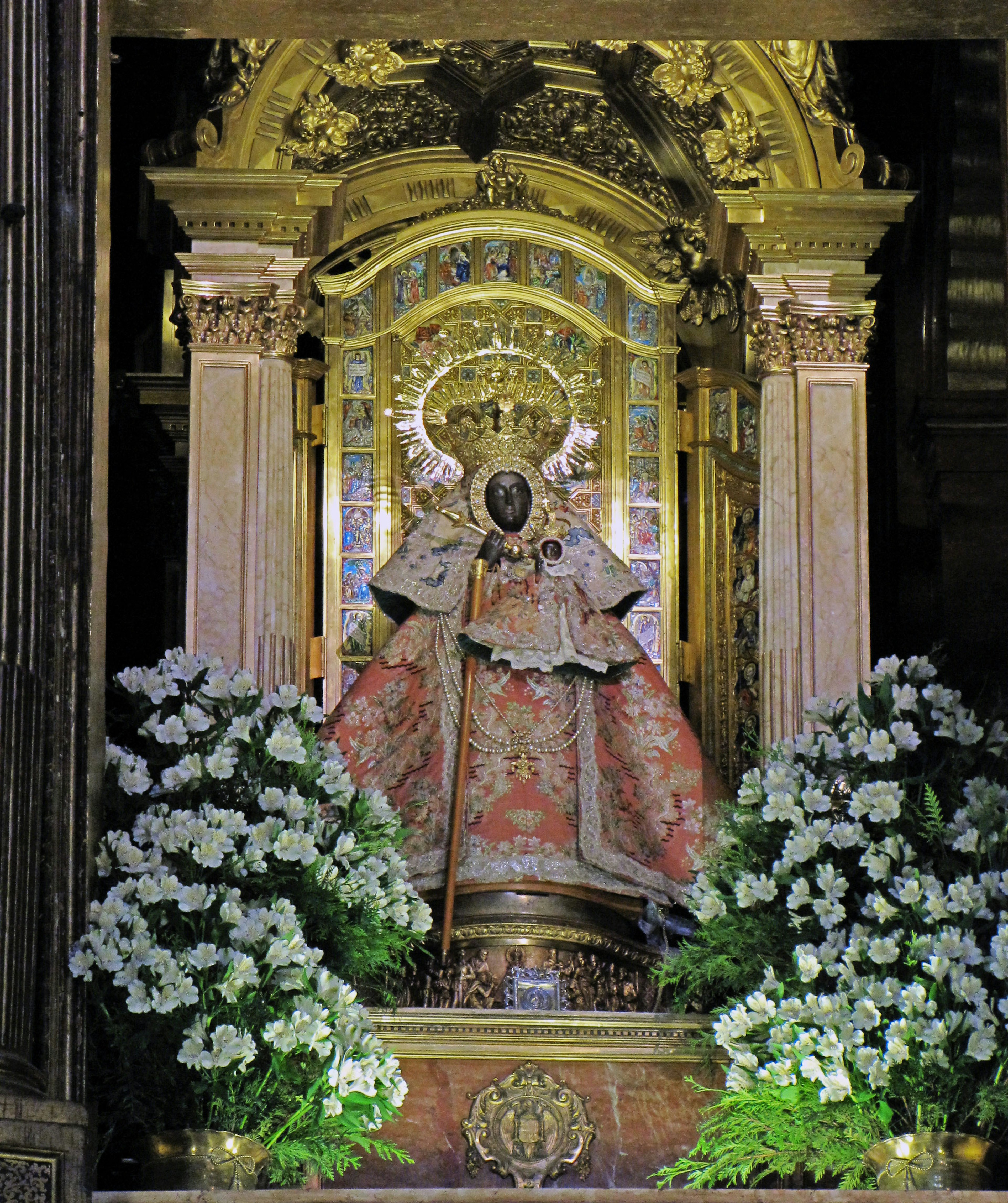 Estatua bellamente decorada en un altar ornamentado rodeada de flores blancas