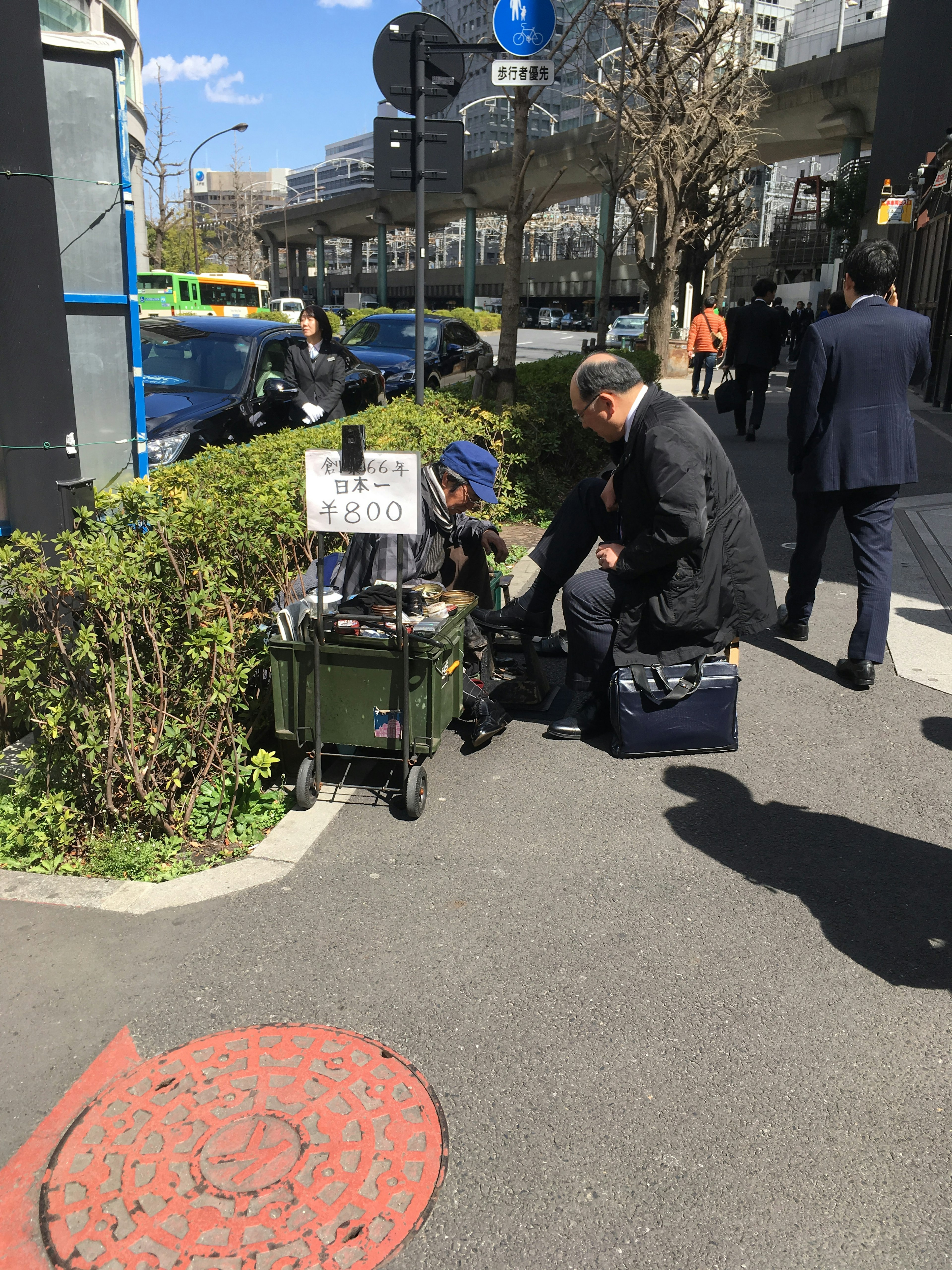 A man organizing items on a cart in an urban sidewalk with green bushes