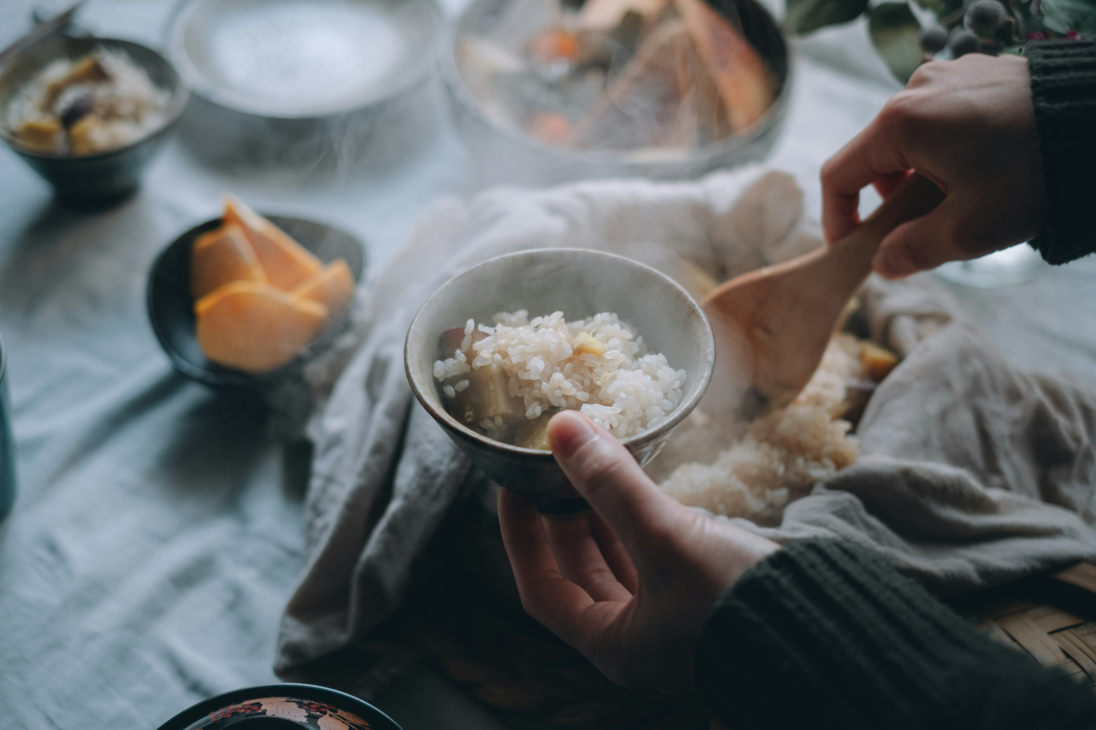 A hand serving steaming rice from a bowl on a cozy table