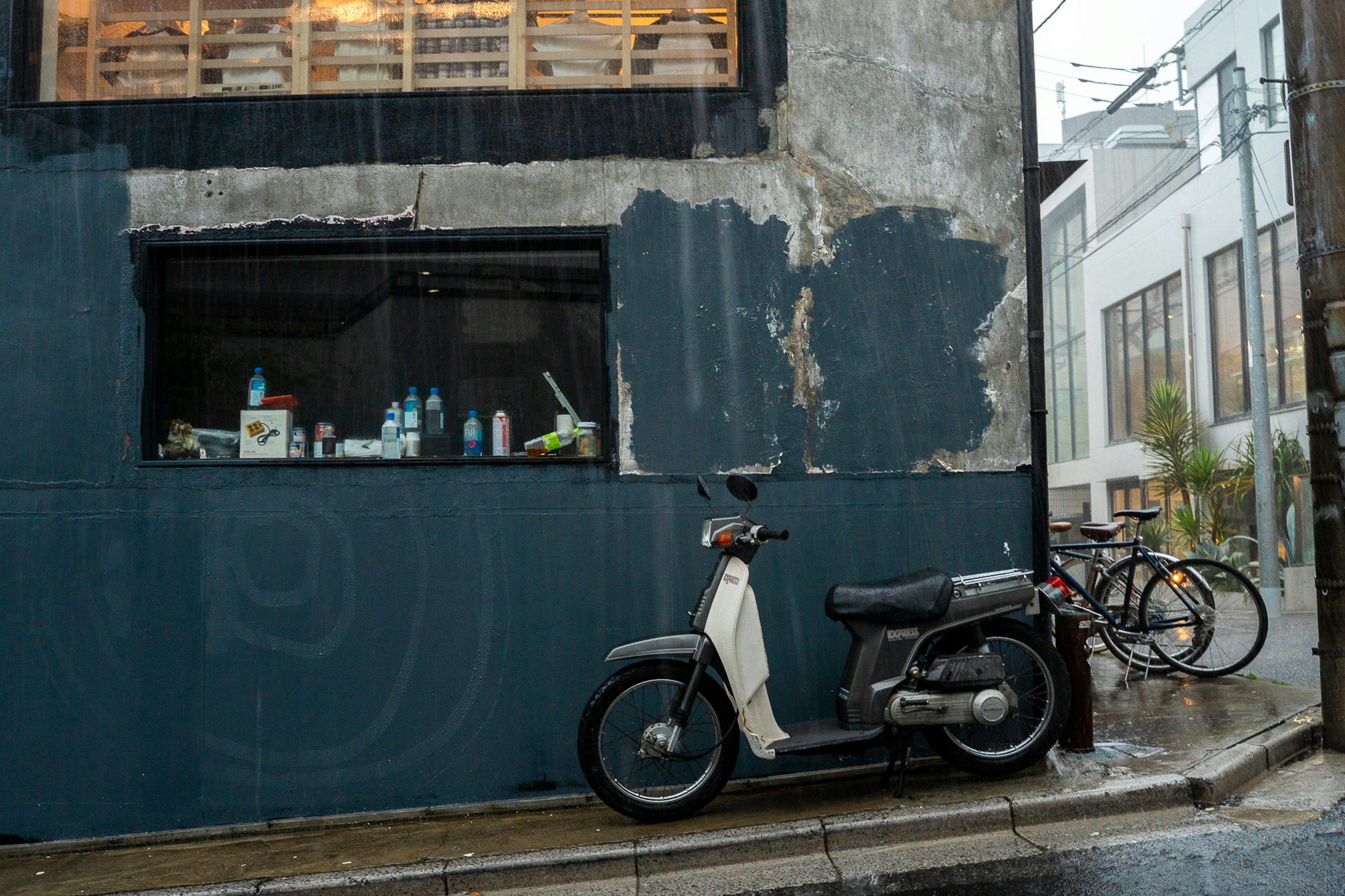 White scooter parked in the rain beside an old building wall