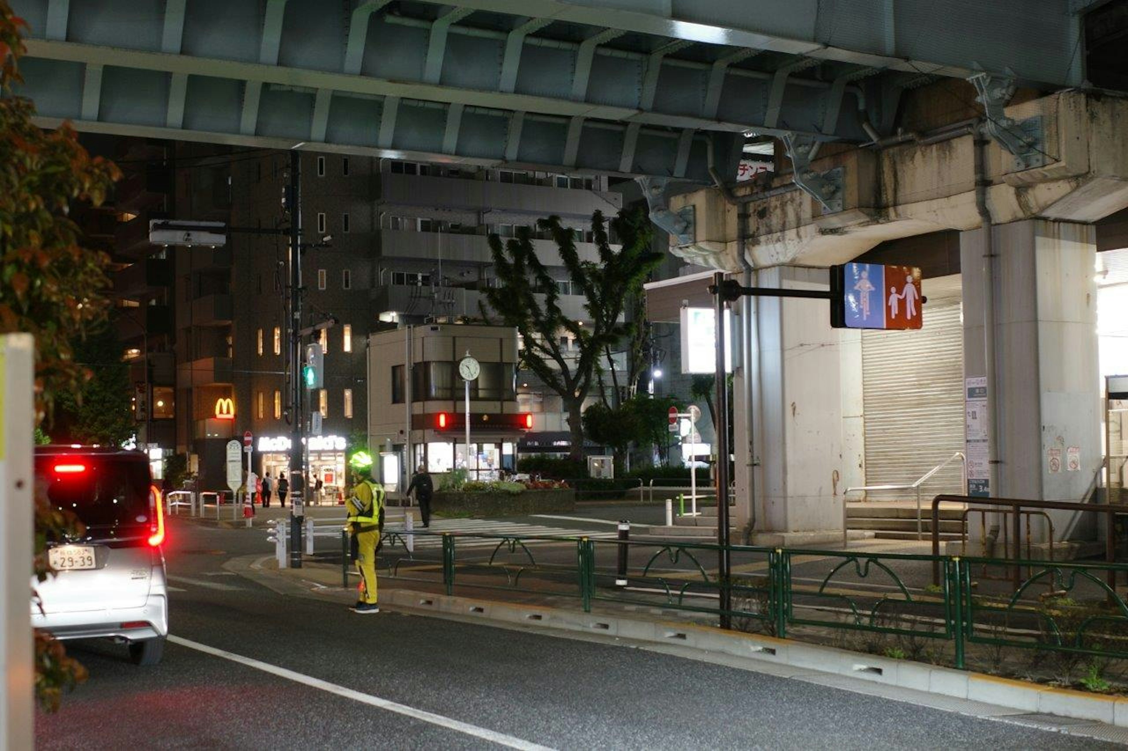 Nighttime cityscape with an elevated structure and street scene showing traffic signals and pedestrians