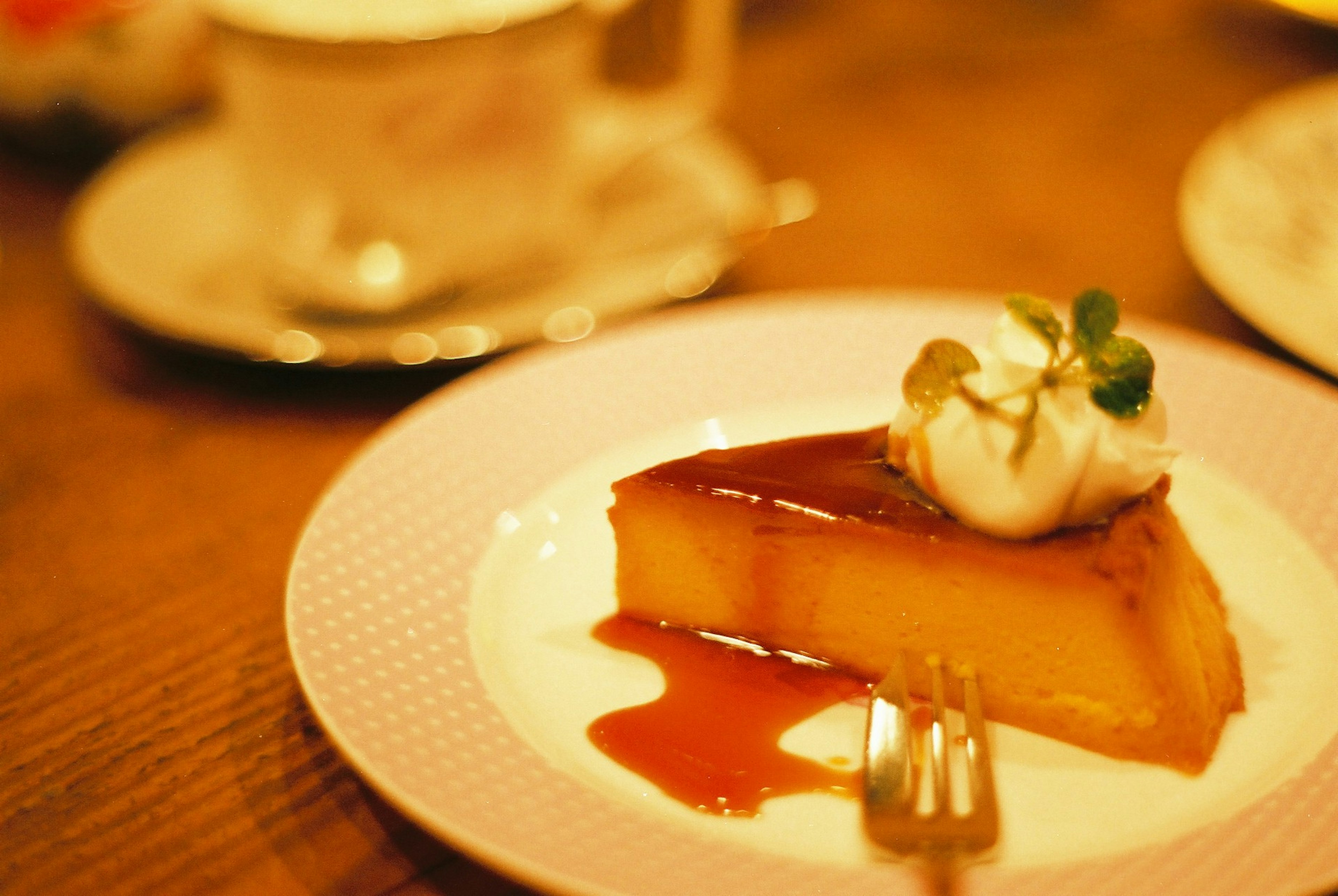 Fetta di flan al caramello guarnita con panna e menta su un piatto decorativo con una tazza di caffè sullo sfondo