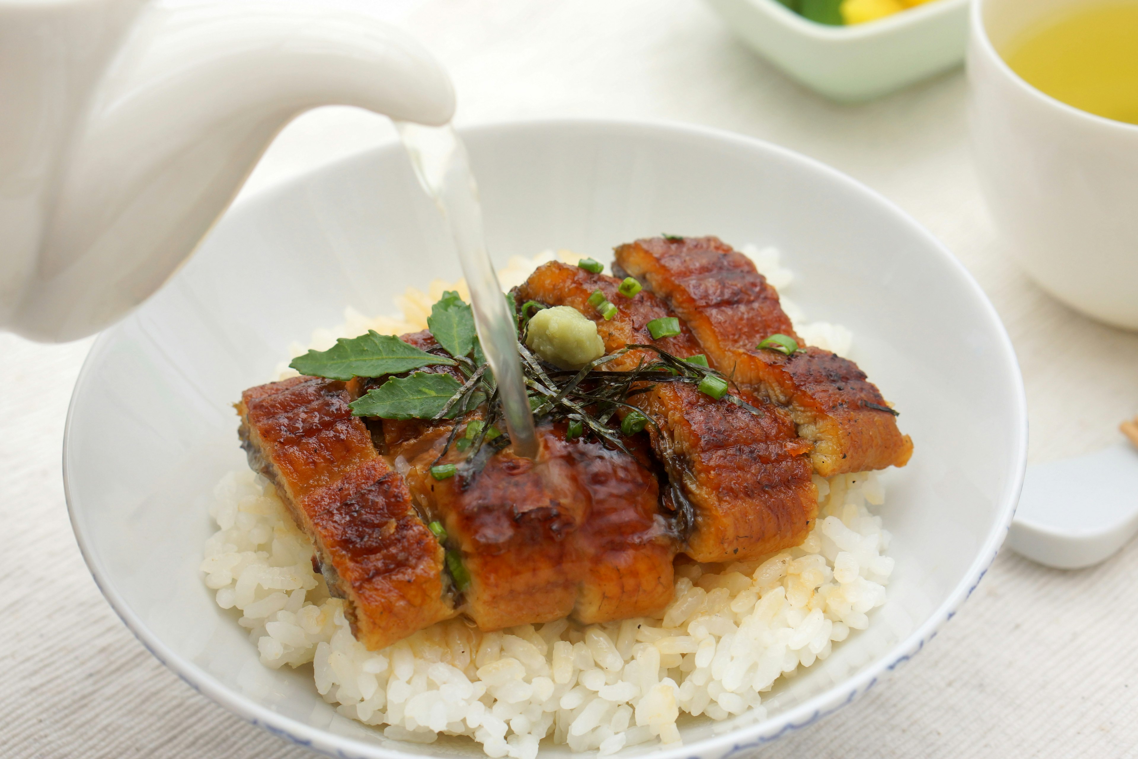 Anguila a la parrilla servida sobre arroz blanco con salsa y decorada con hierbas