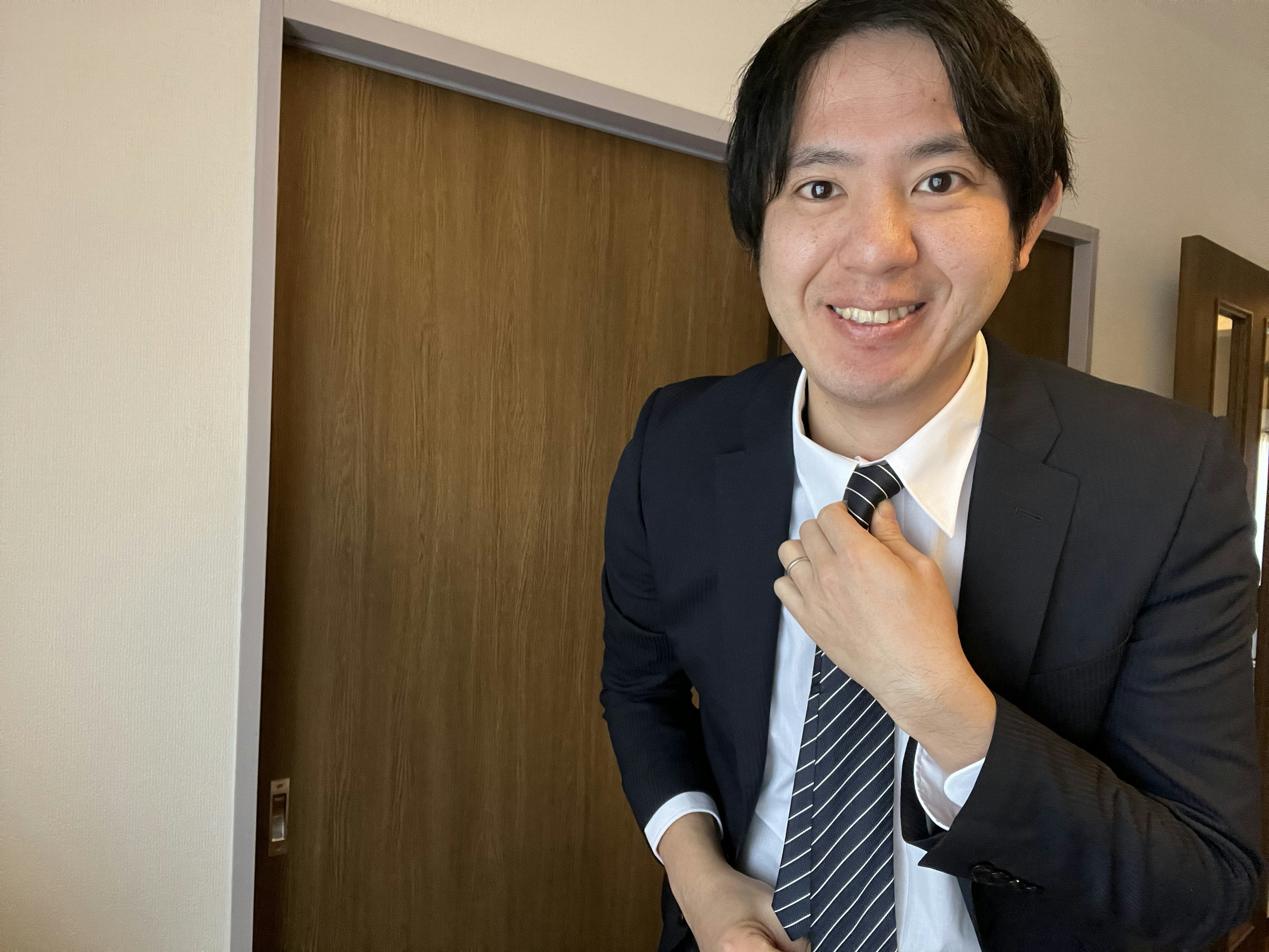 A man in a suit adjusting his tie while smiling in an indoor setting