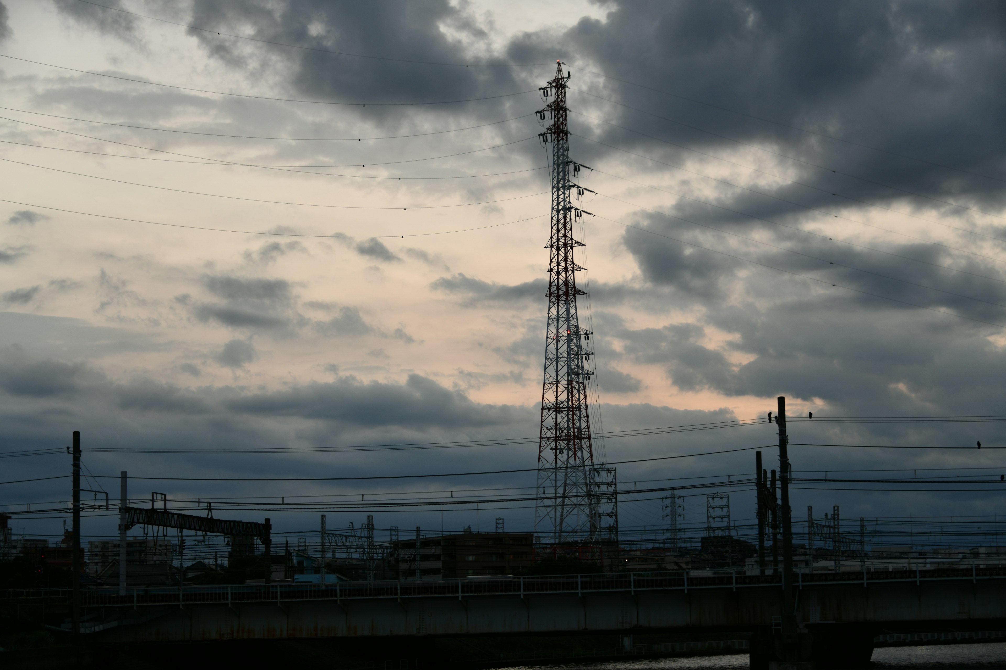 Menara komunikasi tinggi di bawah langit mendung dengan struktur di sekitarnya