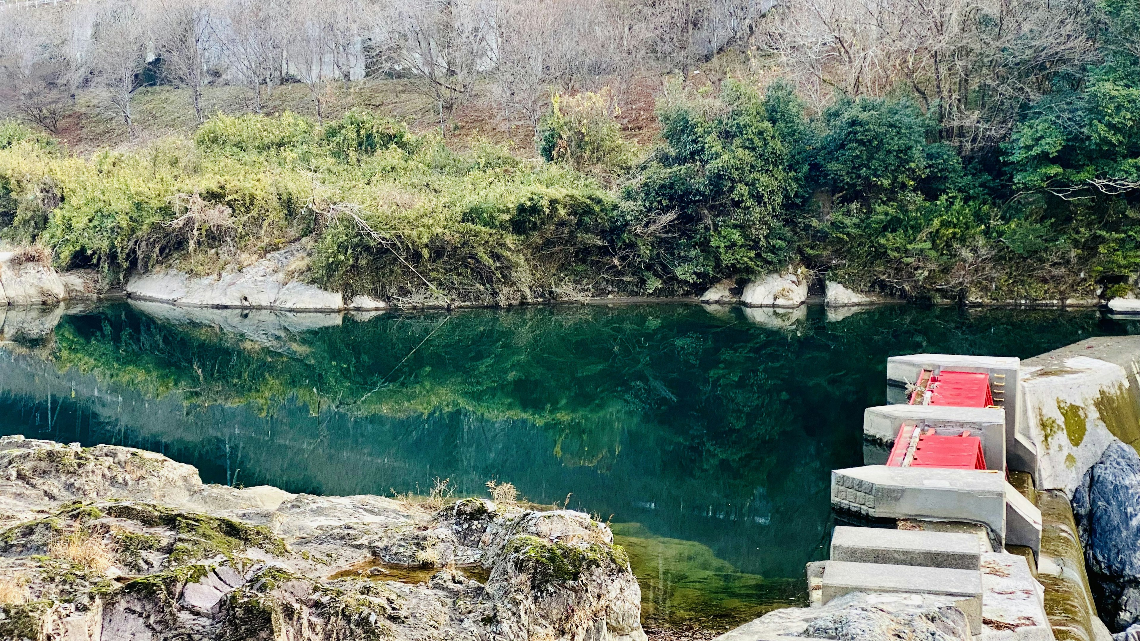 A serene river view featuring red stone steps and lush green vegetation surrounding it