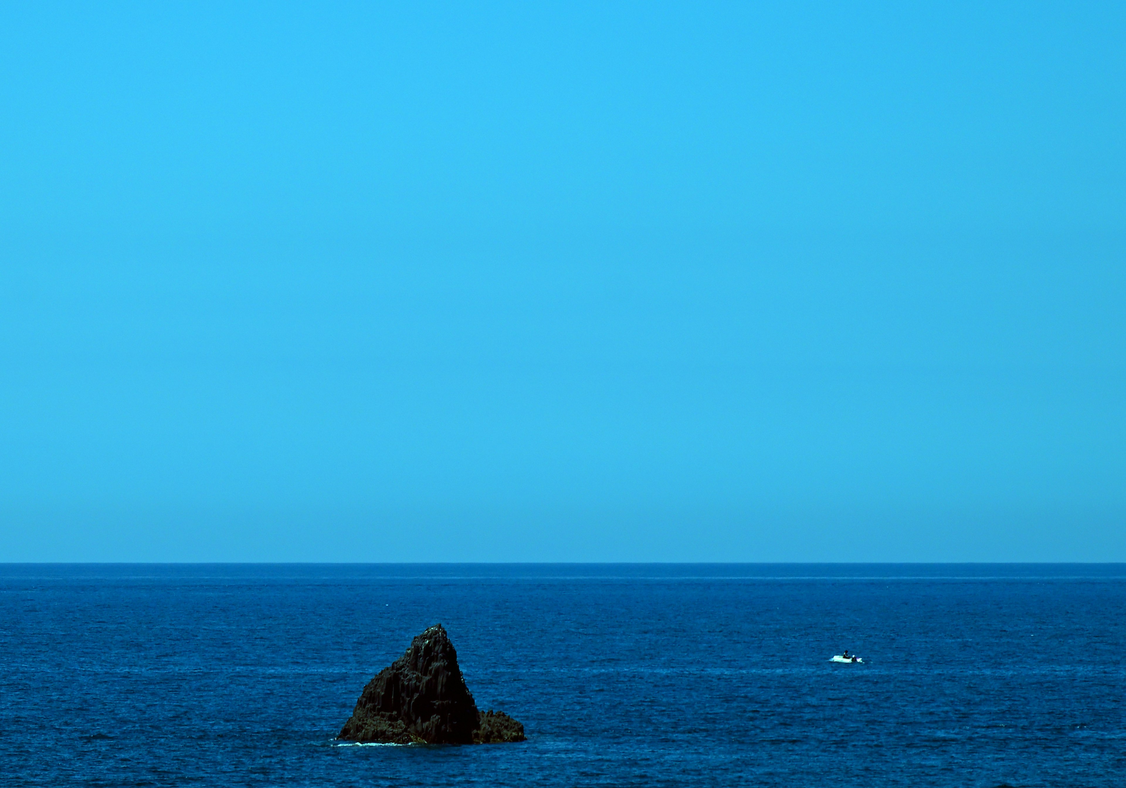 Eine ruhige Aussicht auf das blaue Meer und den Himmel mit einem kleinen Felsen und einem Boot