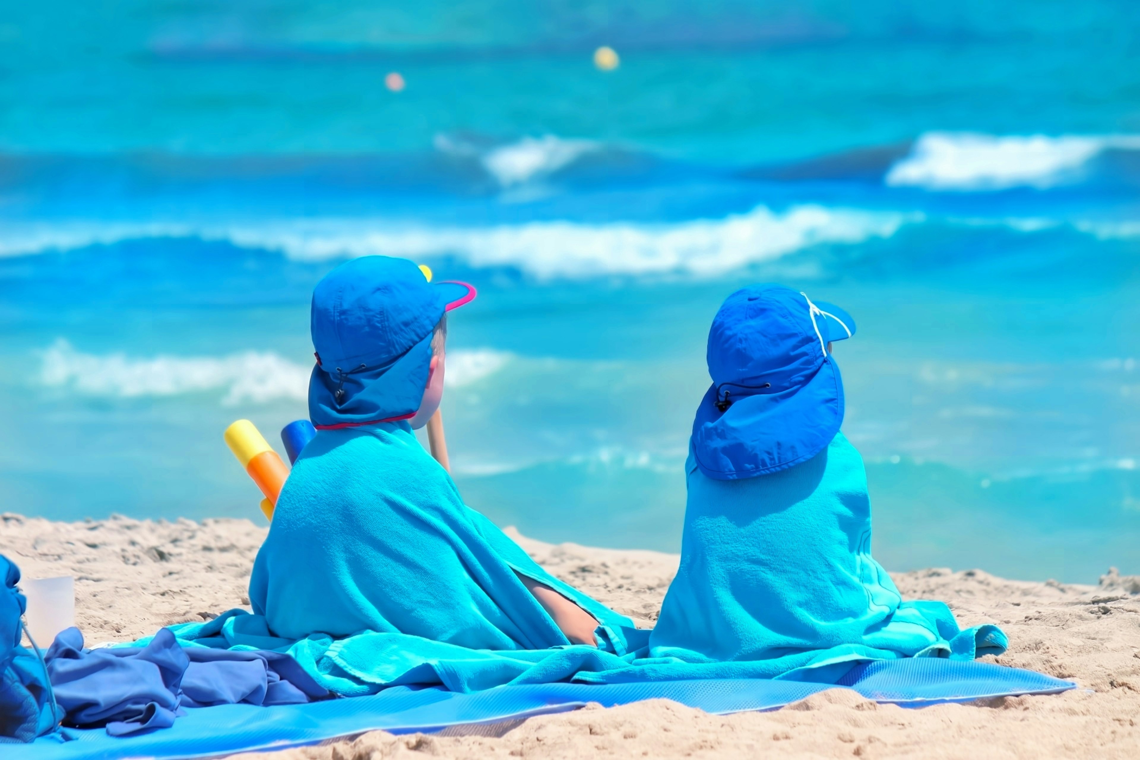 Dos niños sentados en toallas de playa azules mirando el océano