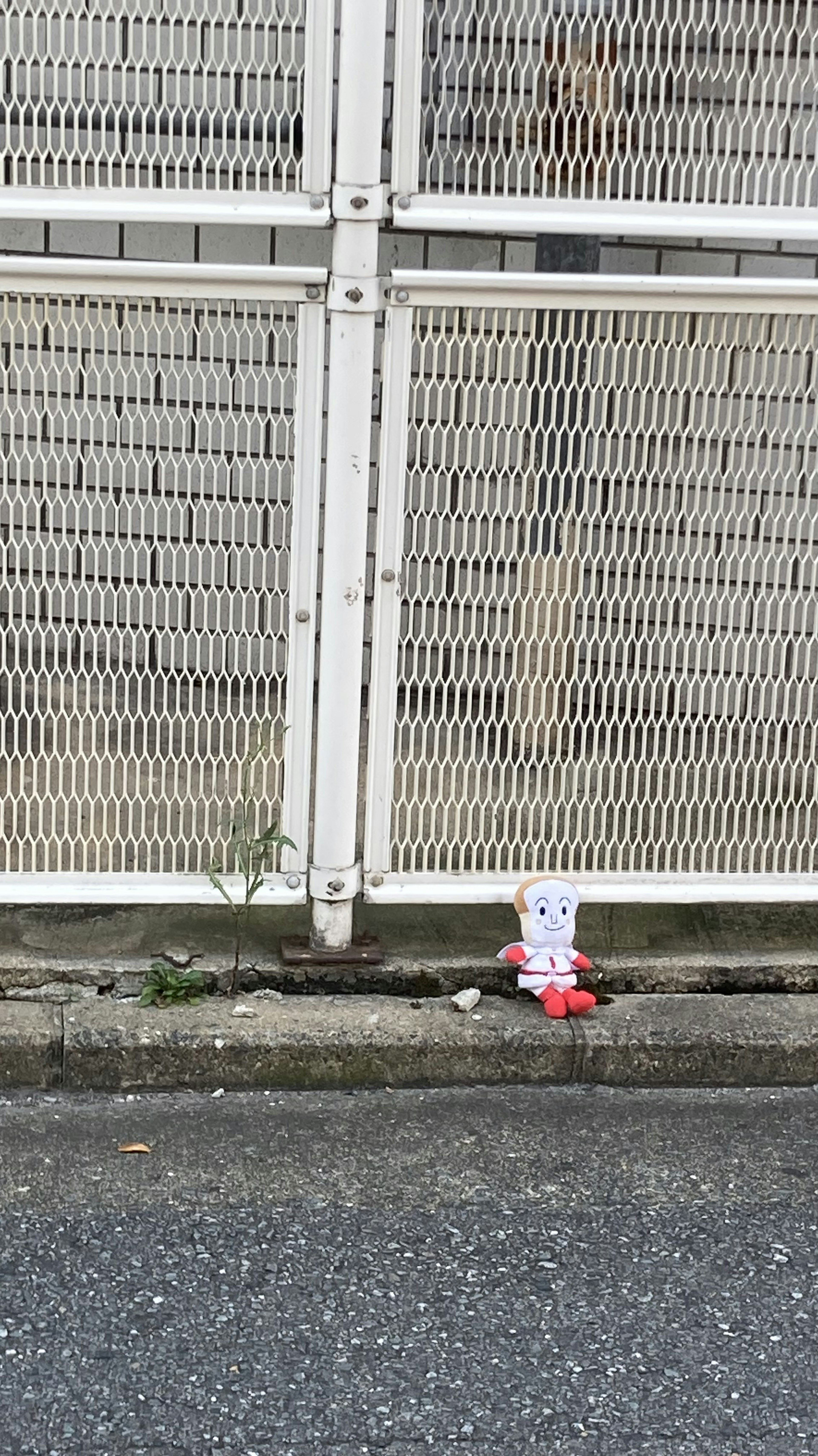 A small doll wearing red clothing placed in front of a white fence