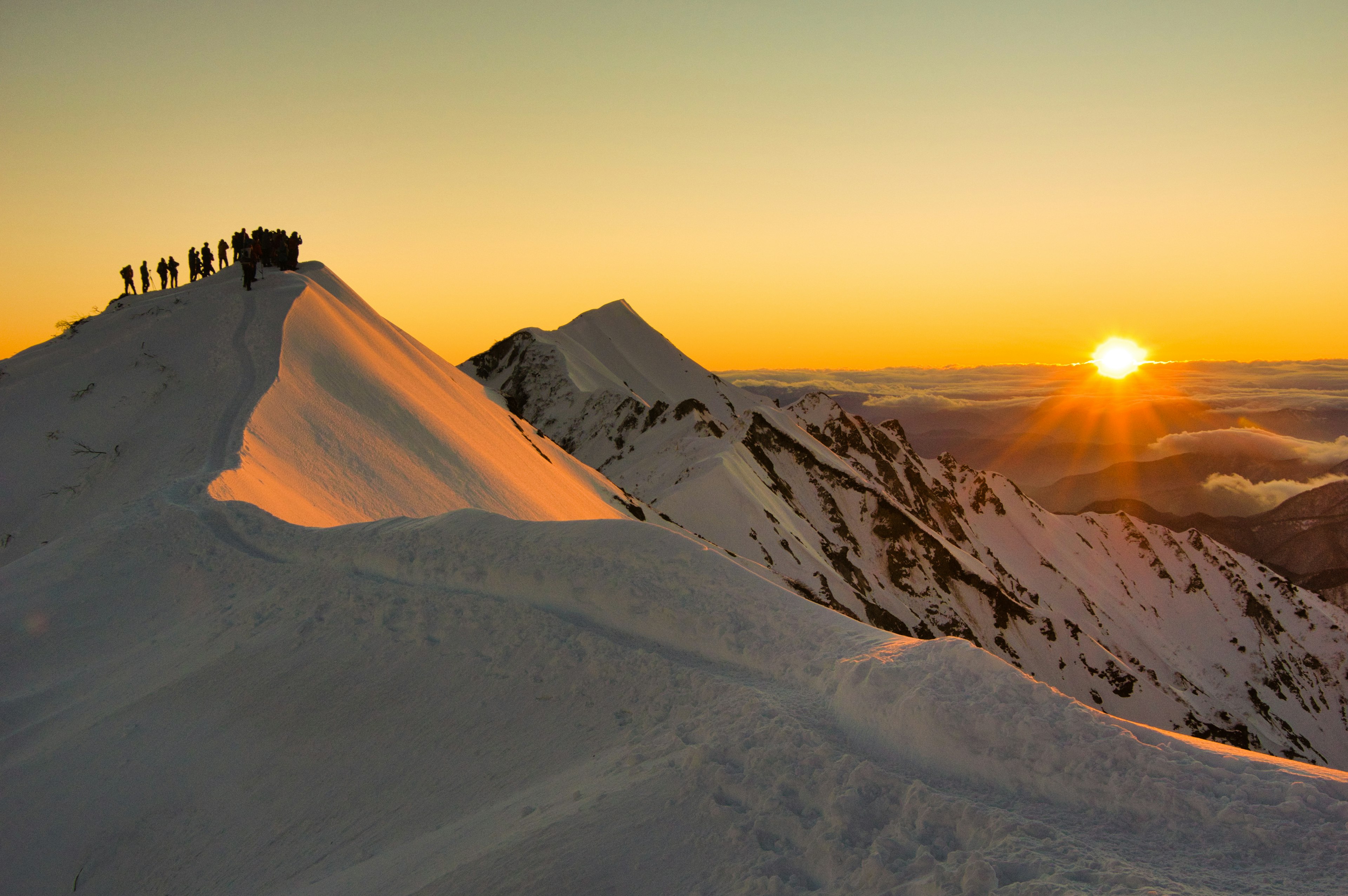 Des gens debout sur un sommet enneigé au coucher du soleil