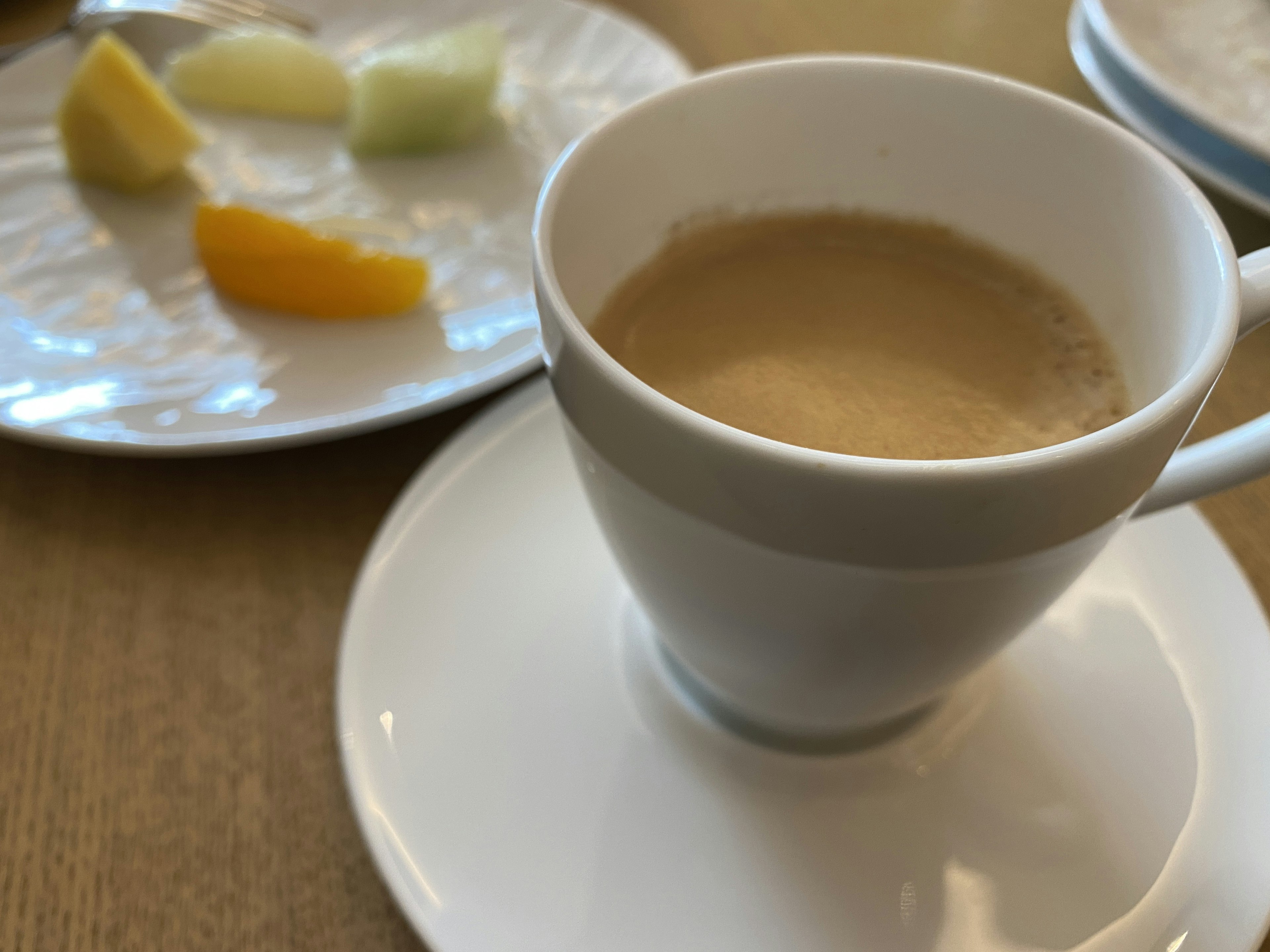 White cup of coffee with a small plate of assorted fruits