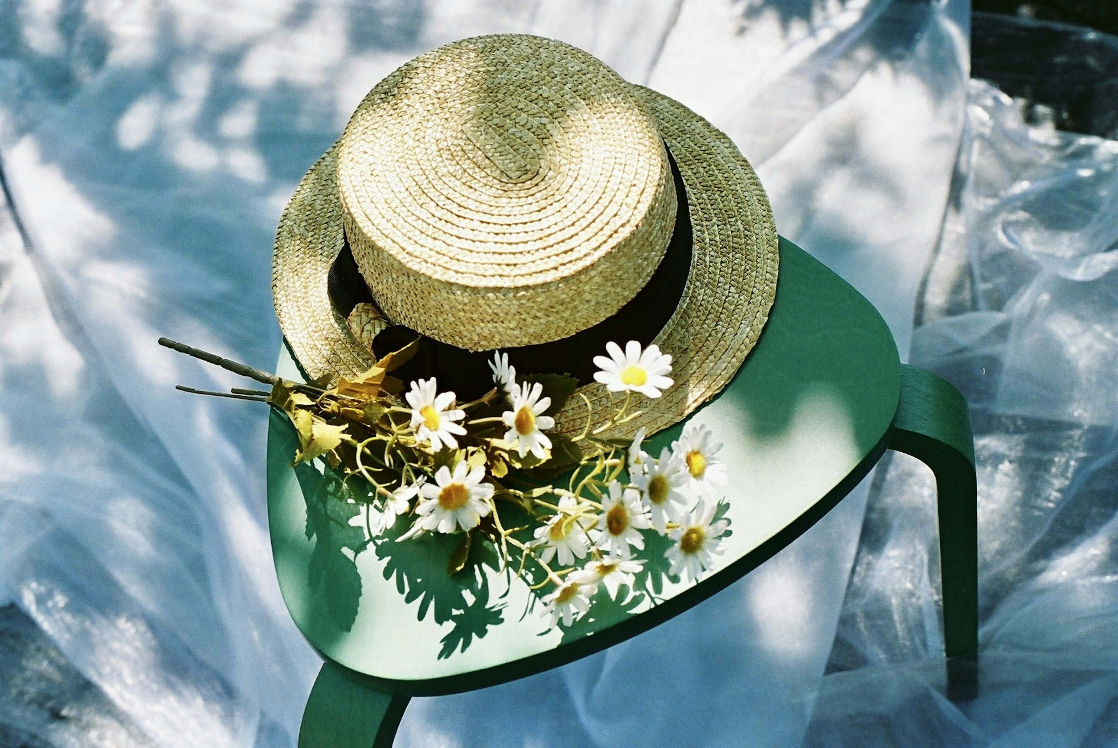 Sombrero de paja colocado sobre una silla verde con arreglo de flores blancas