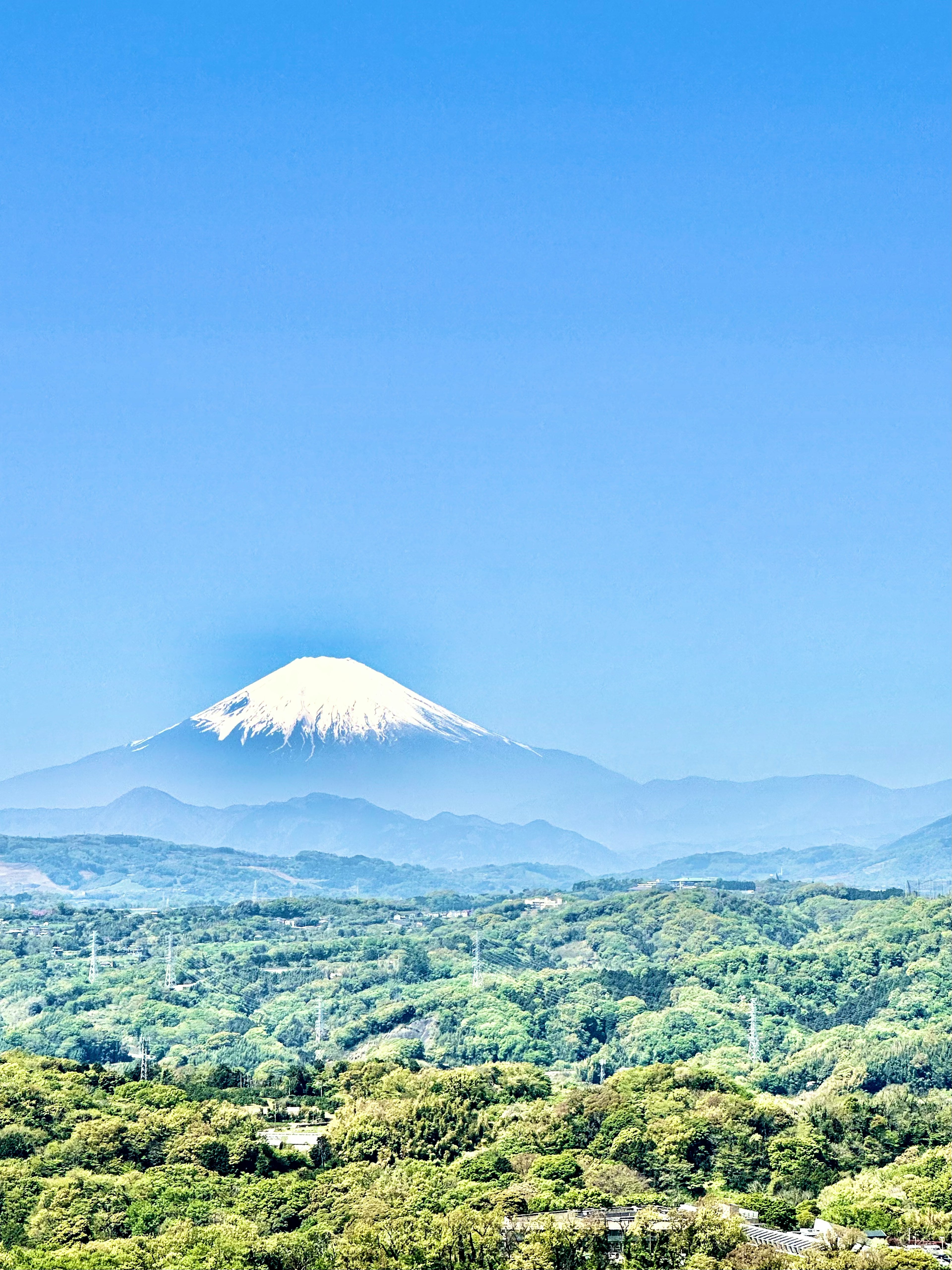 Monte Fuji cubierto de nieve bajo un cielo azul claro con montañas verdes