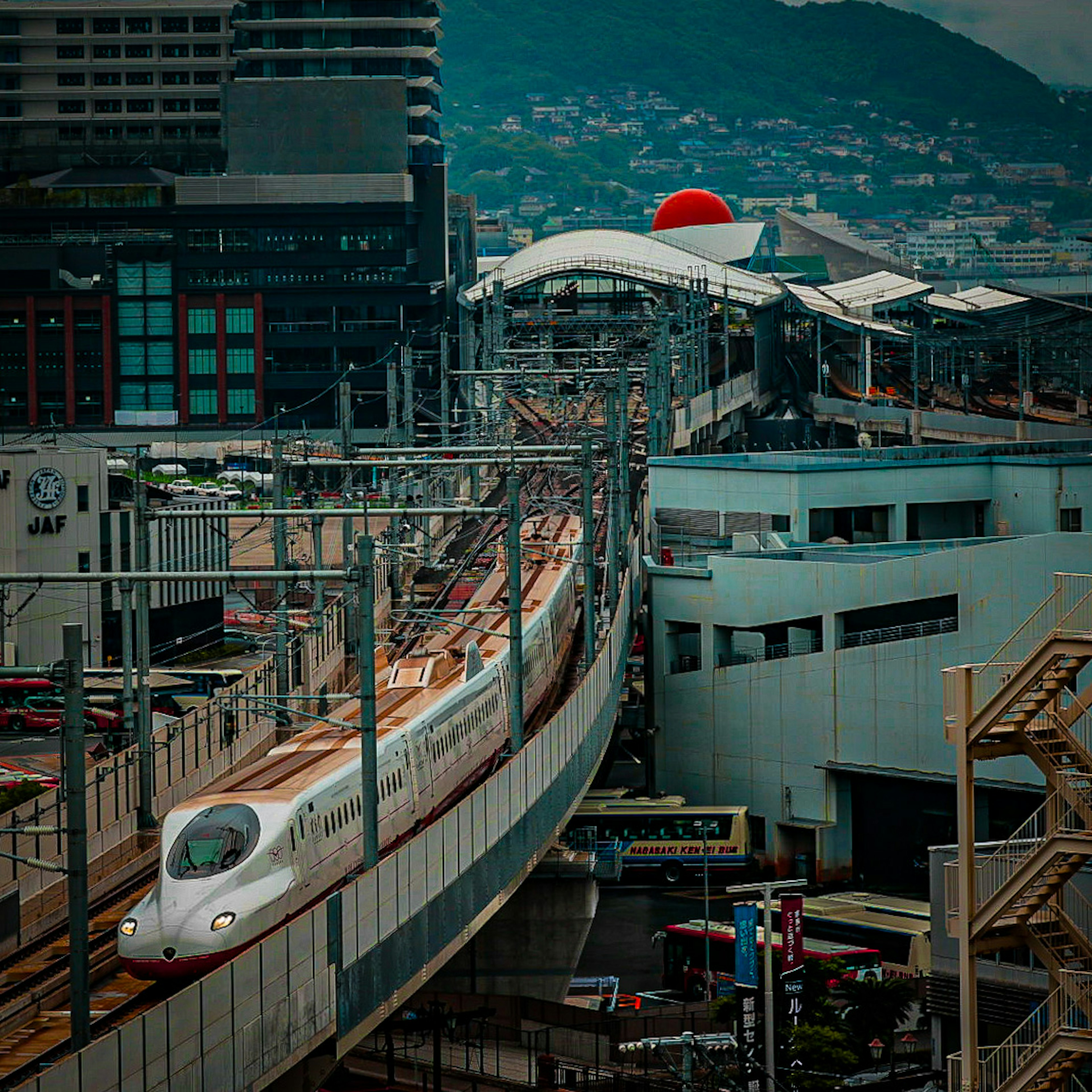 新幹線が駅に到着する風景 高層ビルと山を背景に 赤い丸の屋根が特徴的