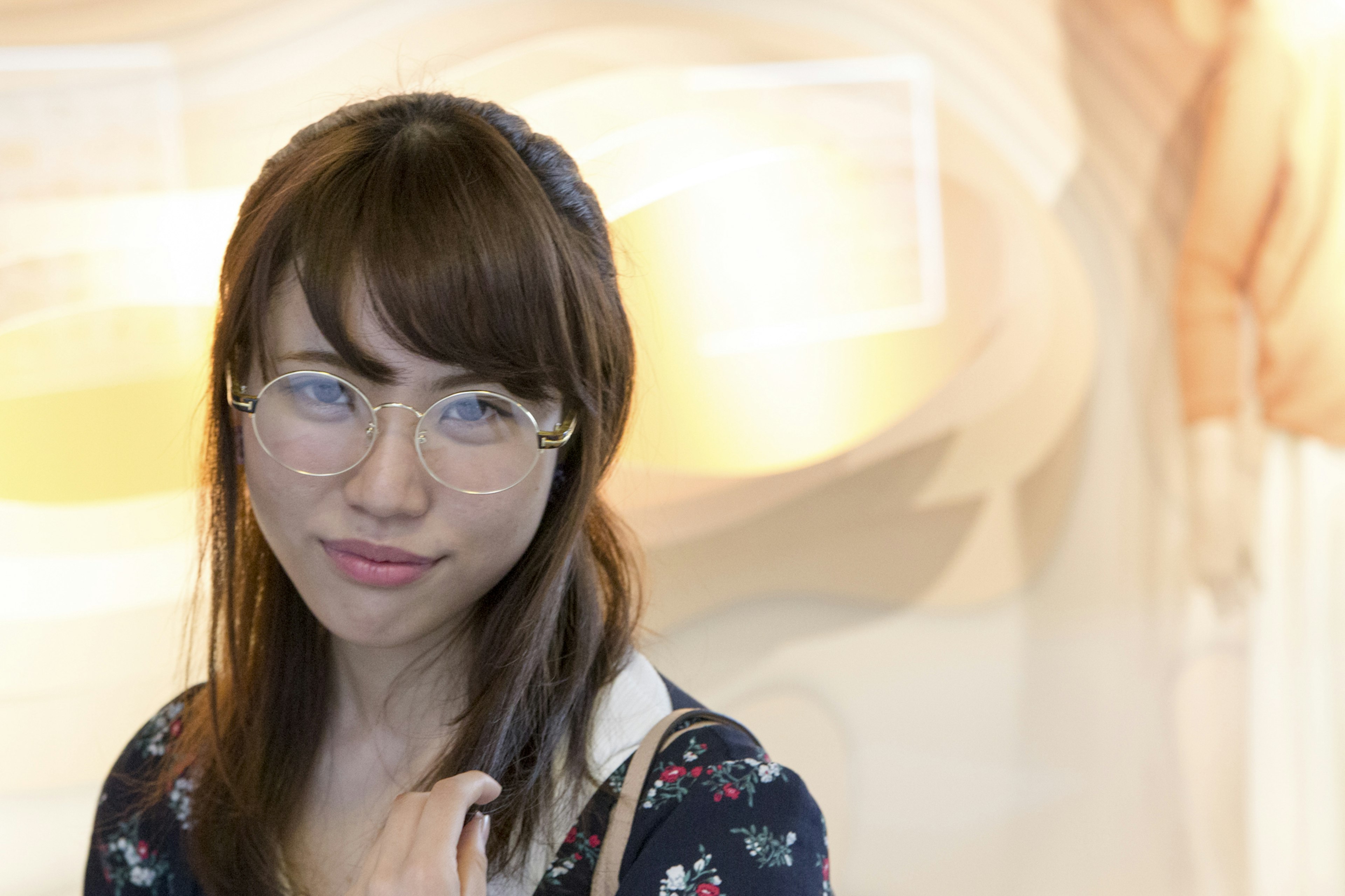 Une femme portant des lunettes souriante avec un arrière-plan aux couleurs douces