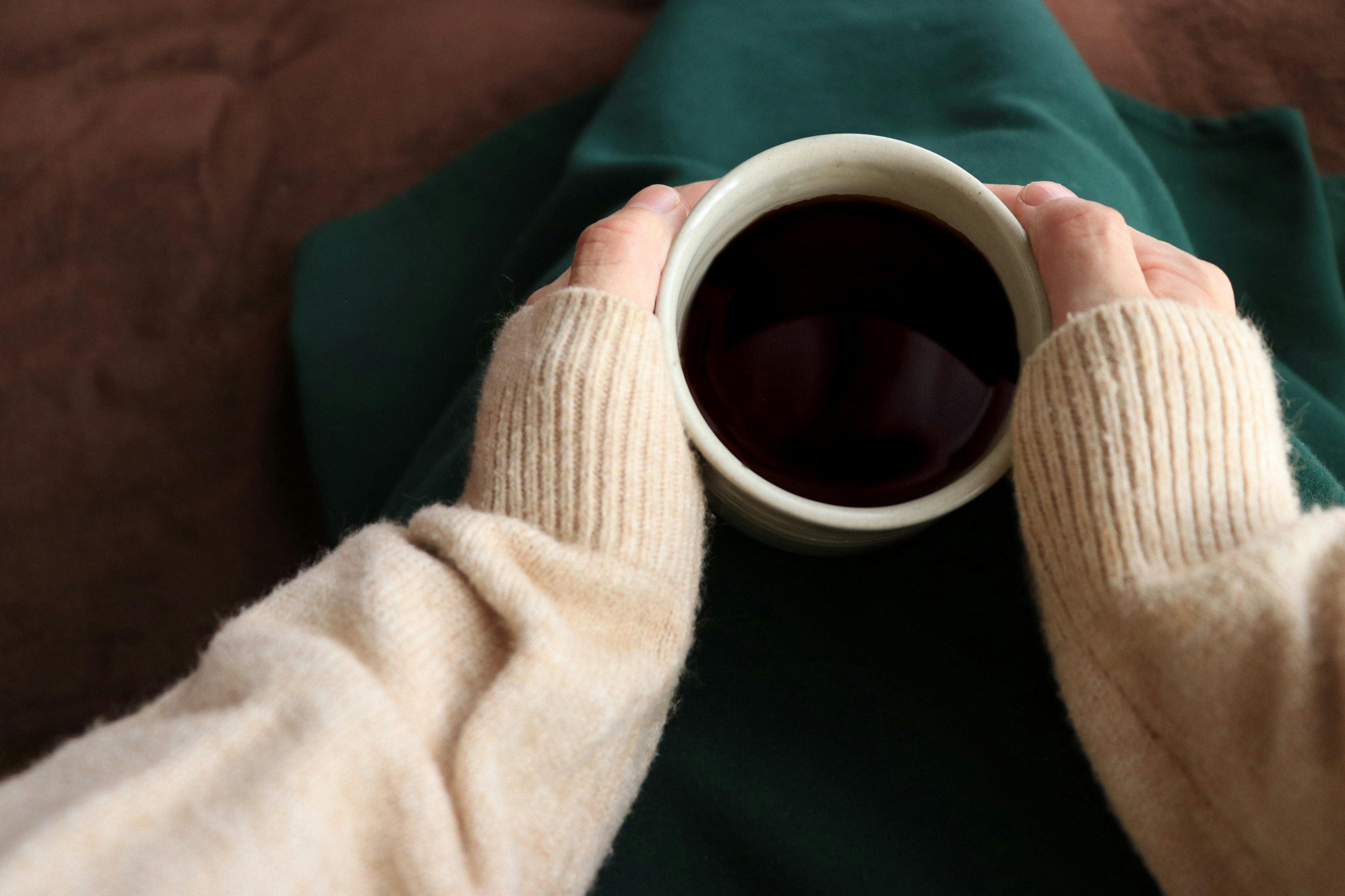 Des mains dans un pull crème tenant une tasse blanche remplie d'une boisson chaude